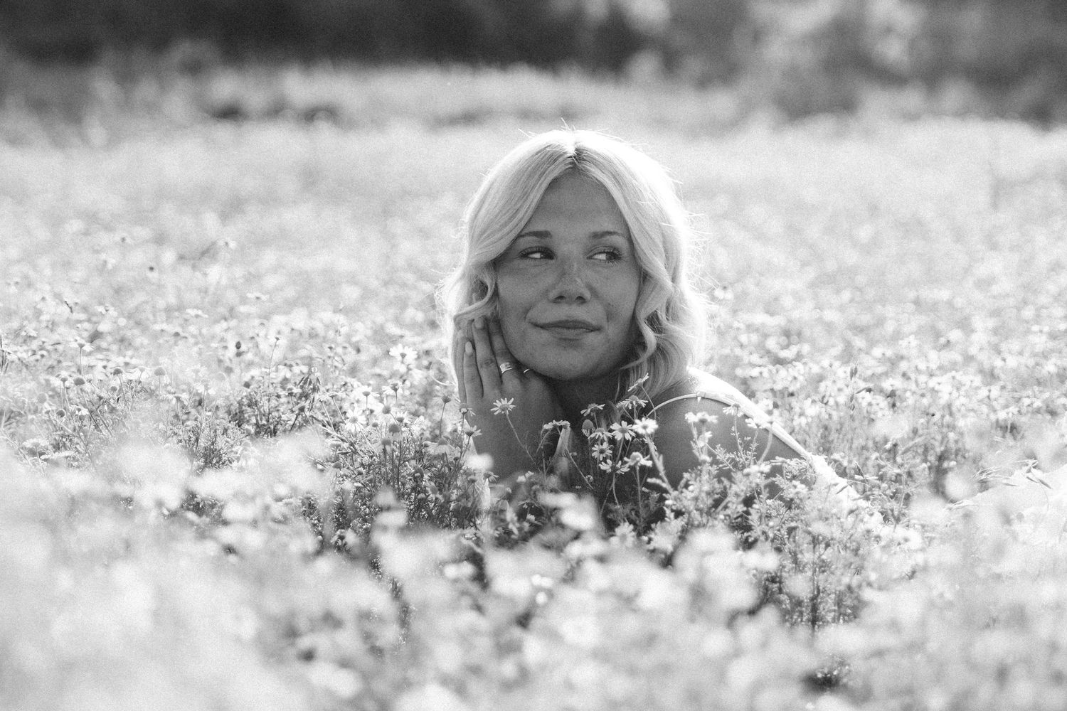 Black and white photo of a blonde woman sitting in a field of wildflowers, gazing upward peacefully.