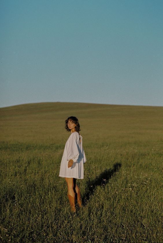 Someone stands in a golden field at sunset casting a long shadow across the grassy landscape.