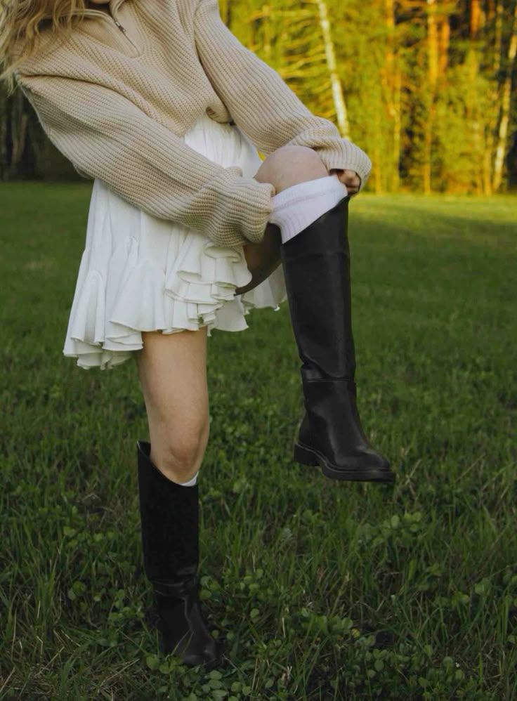 A couple's legs shown in romantic poses against a grassy field with boots and a white dress visible in golden sunlight.