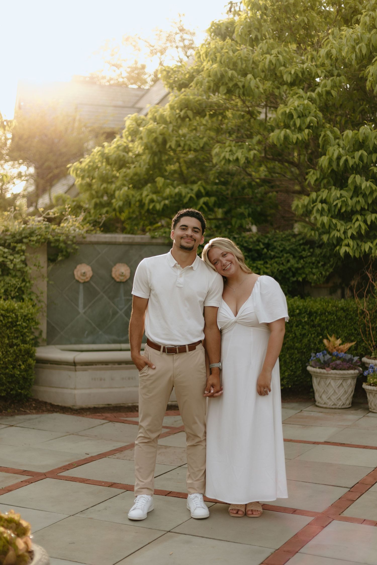 Couple in coordinated white and khaki outfits pose together on stone patio during golden hour.