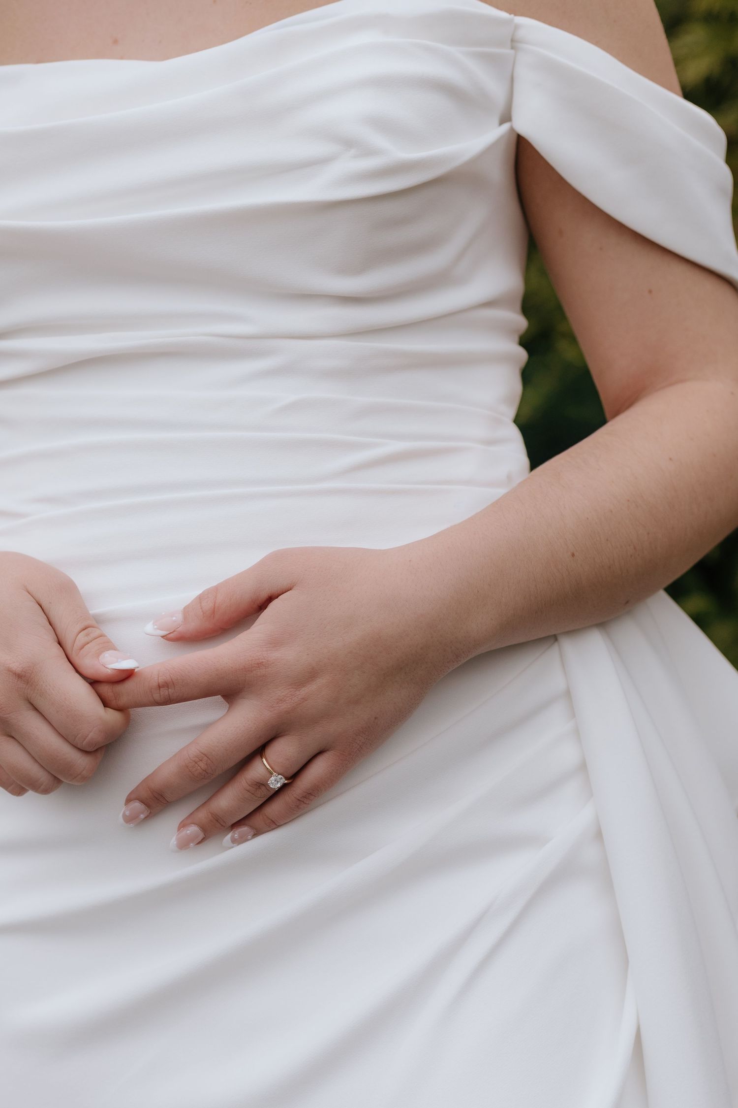 Close-up detail shots of hands wearing a wedding ring against a white dress fabric.