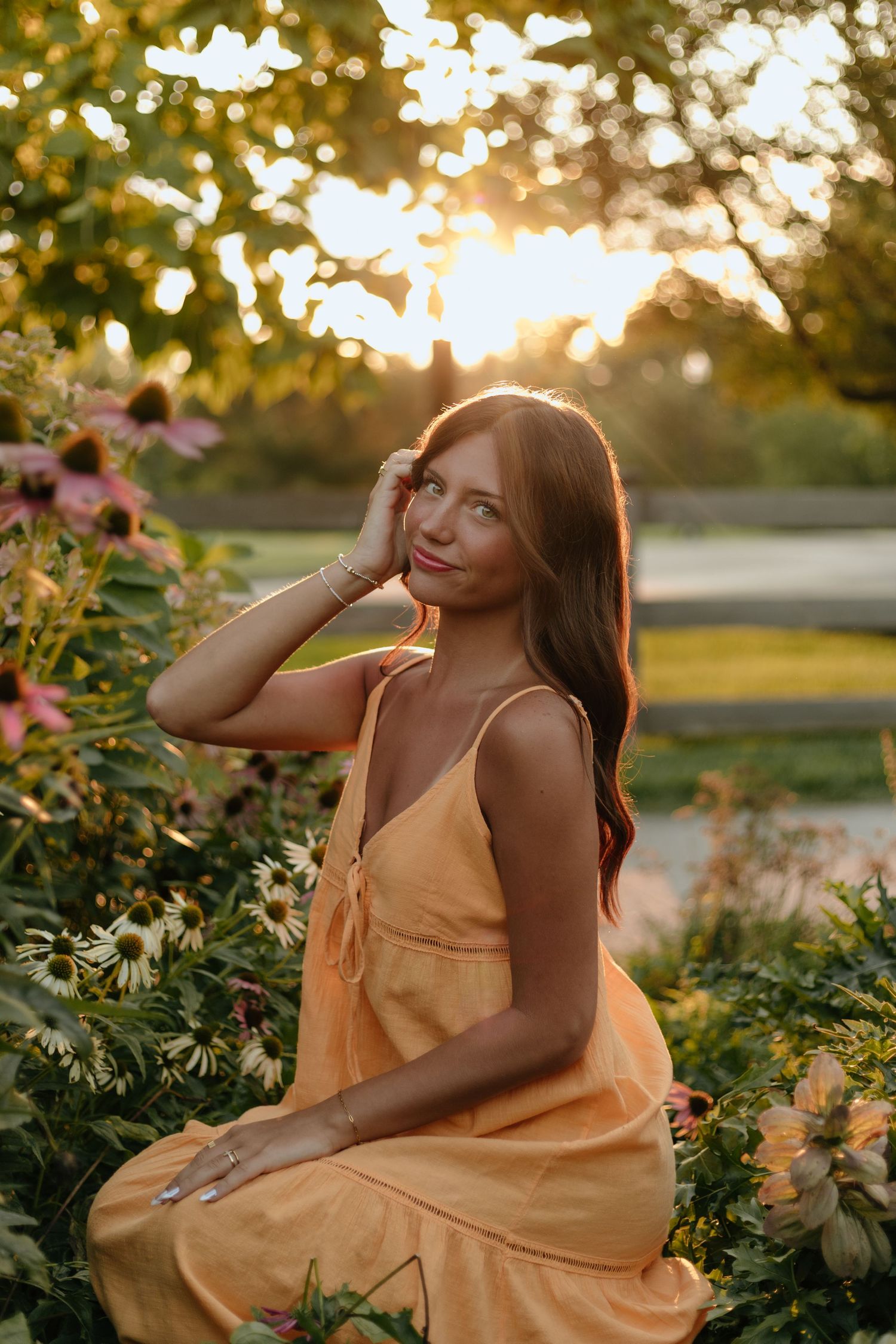 Sunset portrait session in yellow dress among blooming garden flowers with golden light.