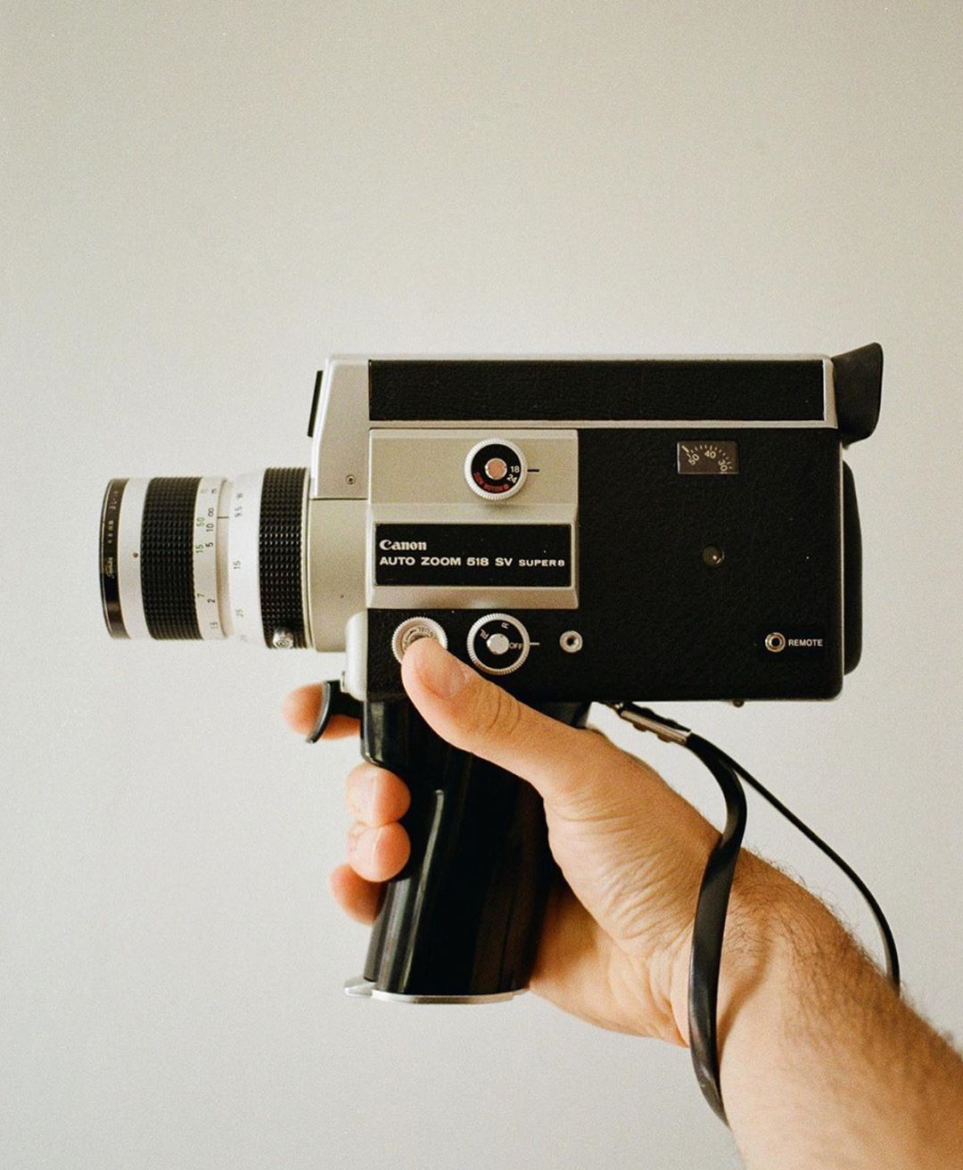 A hand holding a vintage Canon Auto Zoom 8mm Super 8 film camera against a white background.