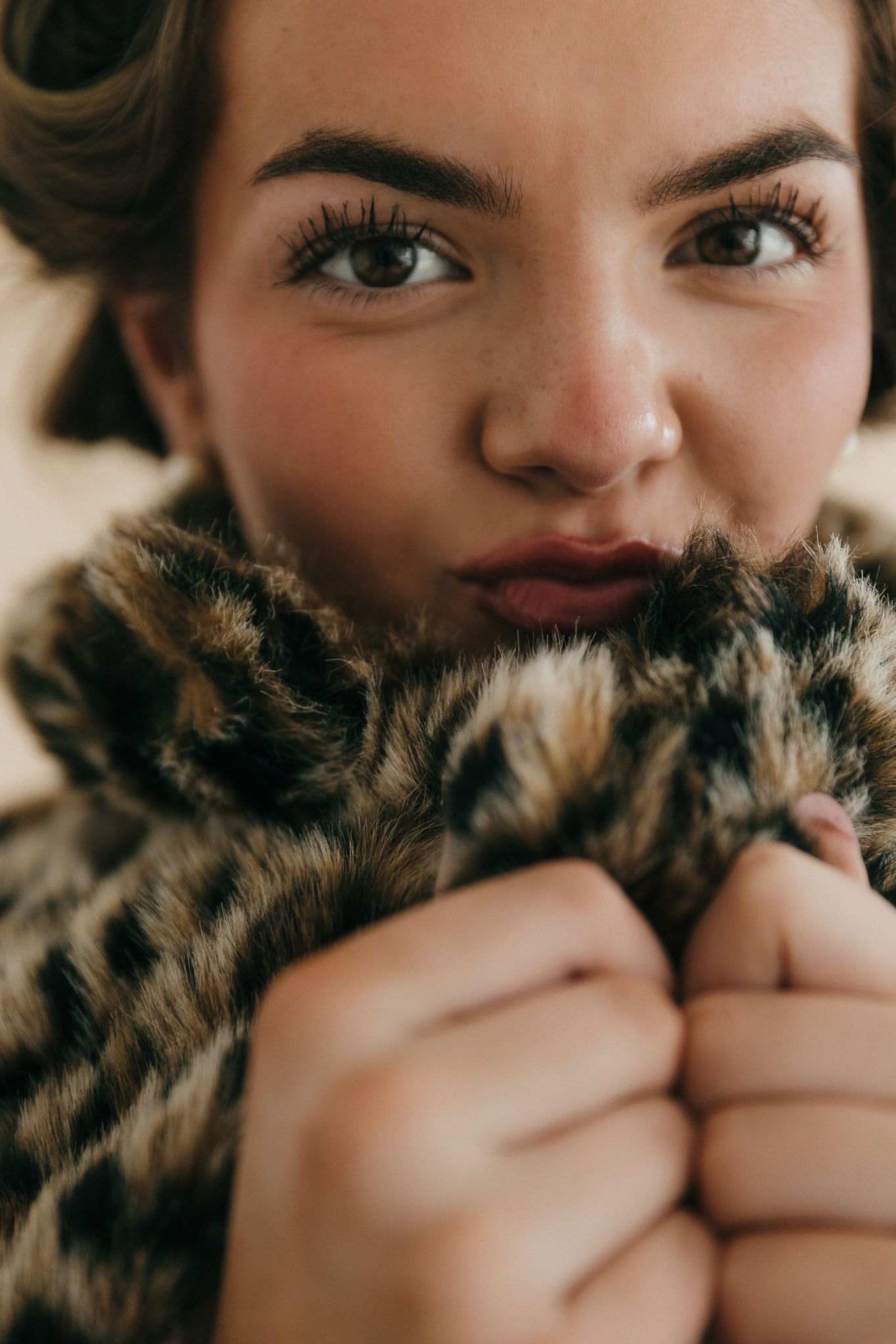 A person's eyes peek playfully over a fluffy brown fur collar in a series of close-up portrait shots.
