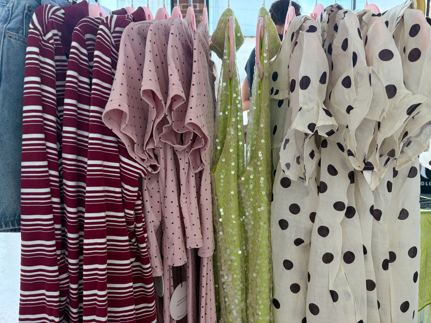 Colorful hanging dresses on a rack featuring stripes, polka dots, and floral patterns in red, pink, green, and cream.