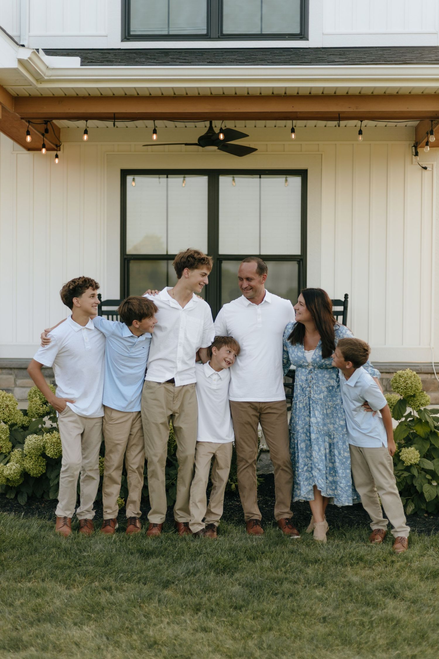 Family group wearing coordinated white and blue outfits poses playfully on lawn.