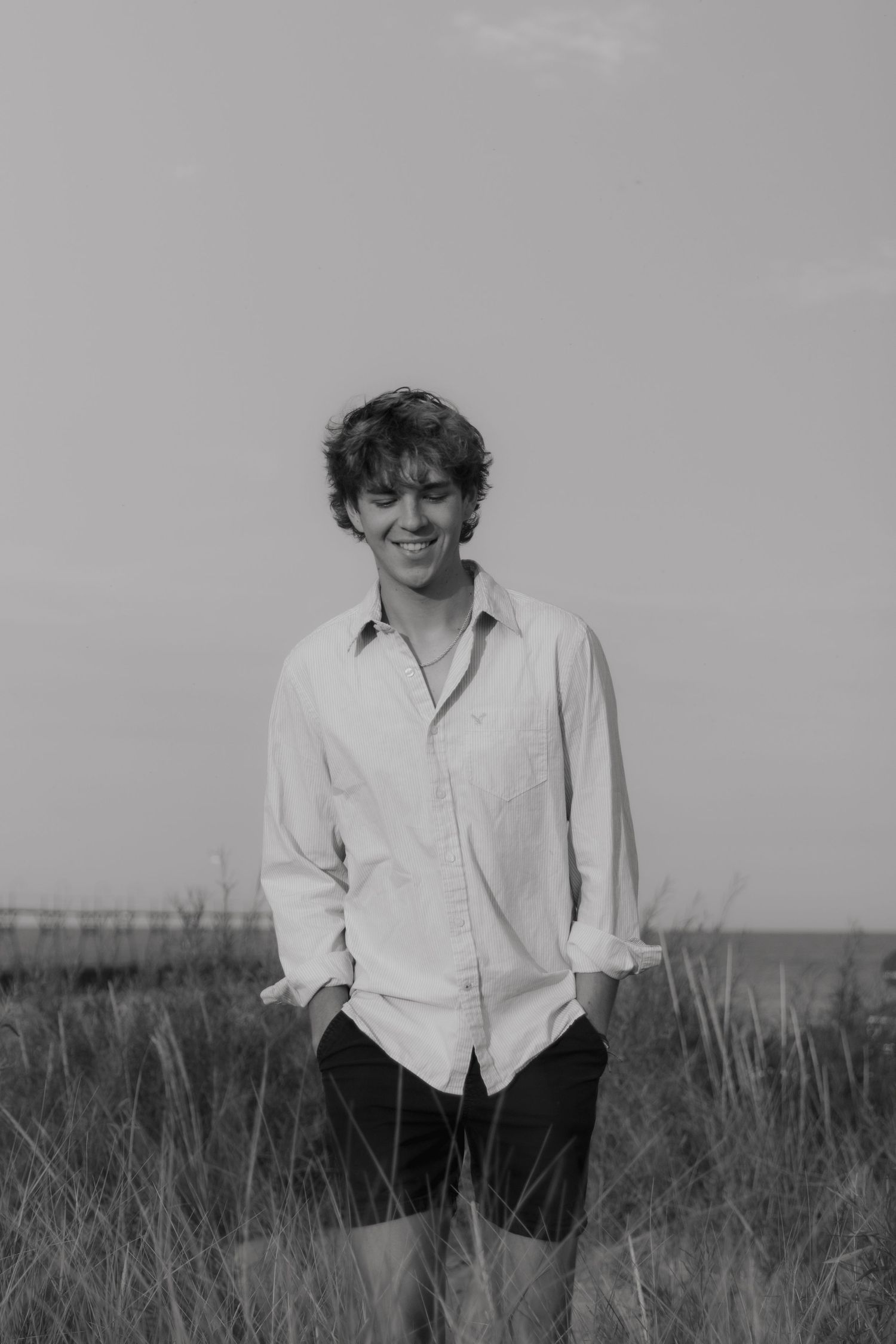 Smiling figure in white shirt photographed in tall grass field on sunny day creating casual outdoor portrait series.