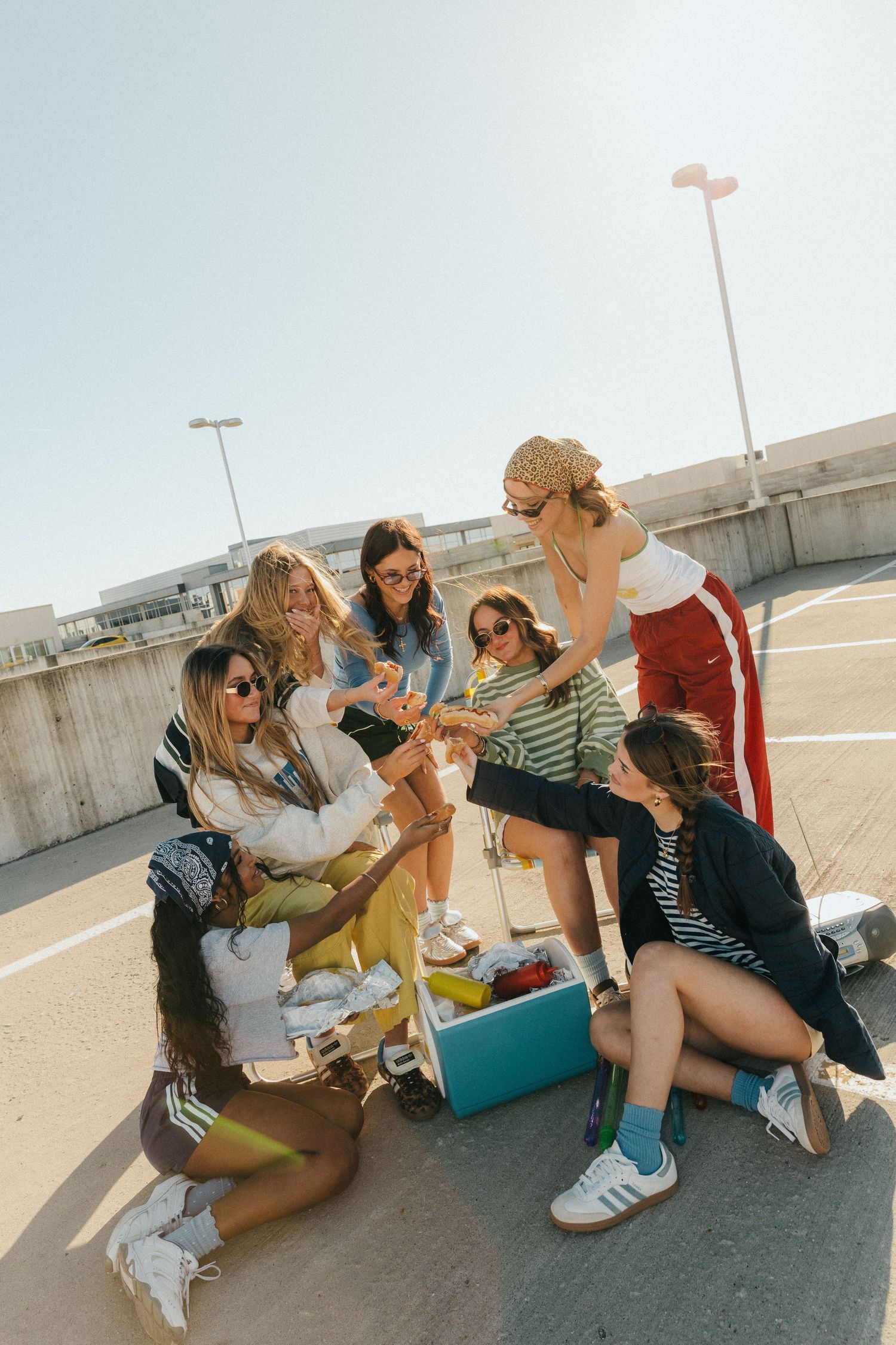Group of young women gathering around a cooler on a sunny rooftop, enjoying drinks and socializing outdoors.