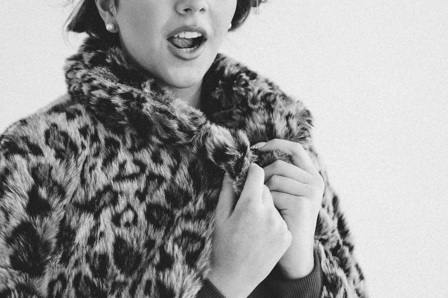 Black and white photo showing someone wearing a leopard print fur coat with an expressive open-mouthed pose.
