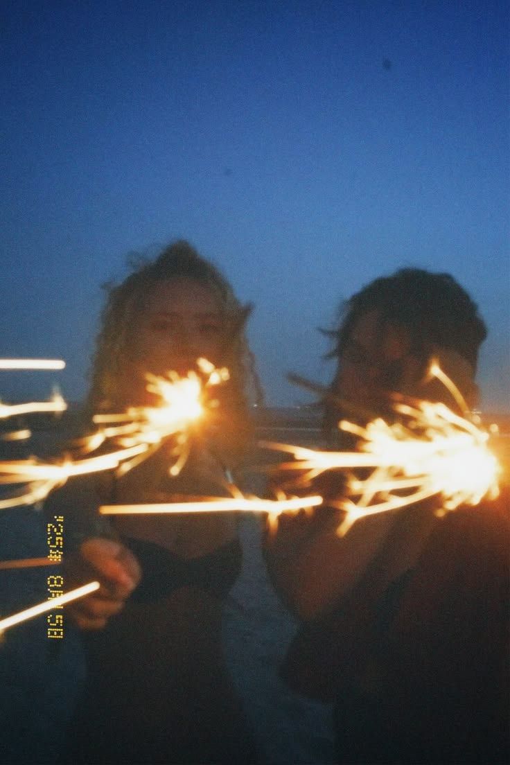 Two people holding sparklers at dusk, creating bright light trails against a deep blue evening sky.