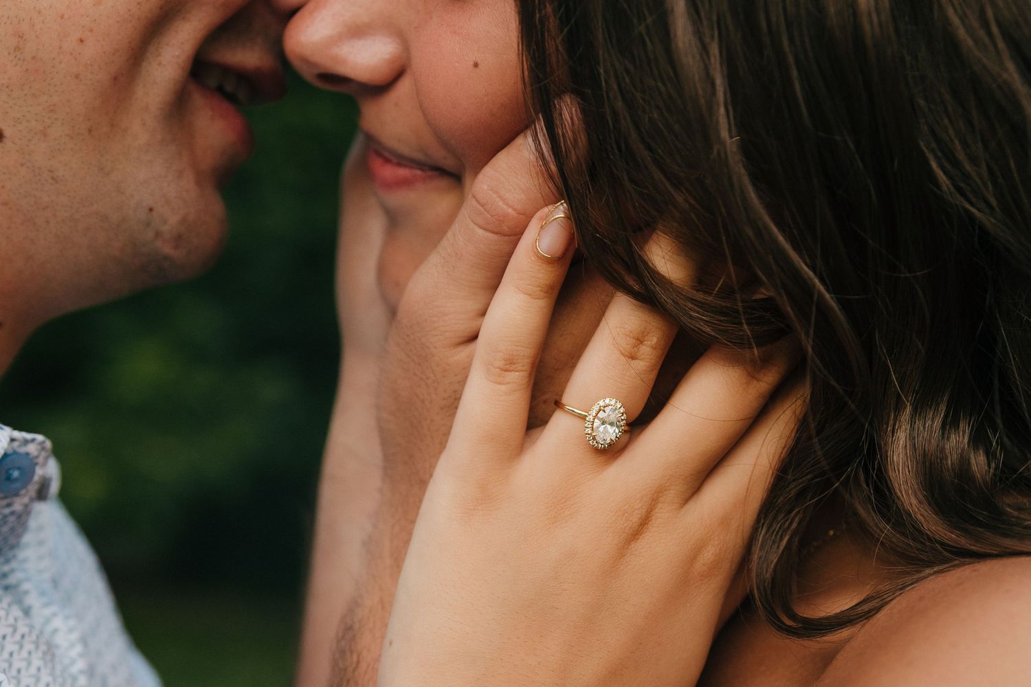 Close-up of a couple sharing a romantic moment, showcasing a stunning oval diamond engagement ring on her hand.