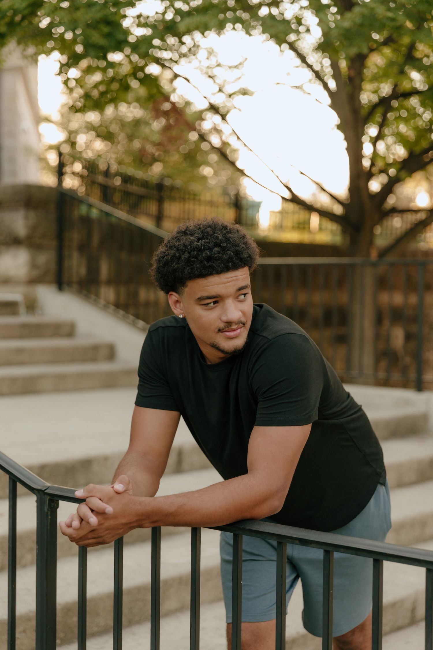 Person in black t-shirt leaning casually against outdoor railing during golden hour.