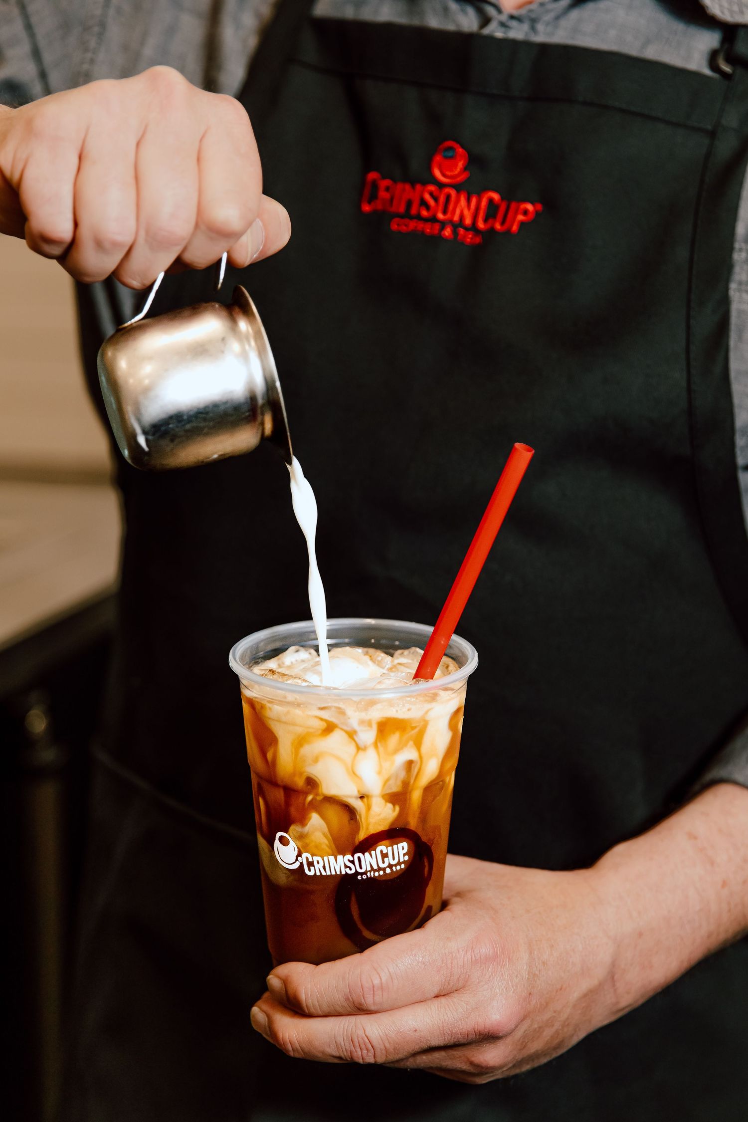 Barista pouring cream into iced coffee drinks with Grindstone Coffee branding.