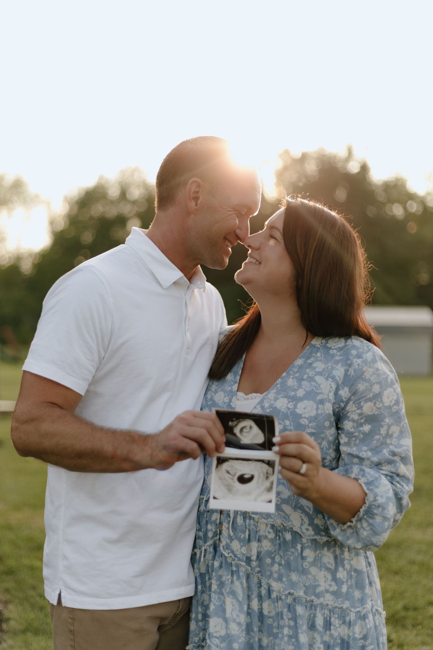 Couple sharing intimate moment while holding ultrasound photo during pregnancy announcement shoot.
