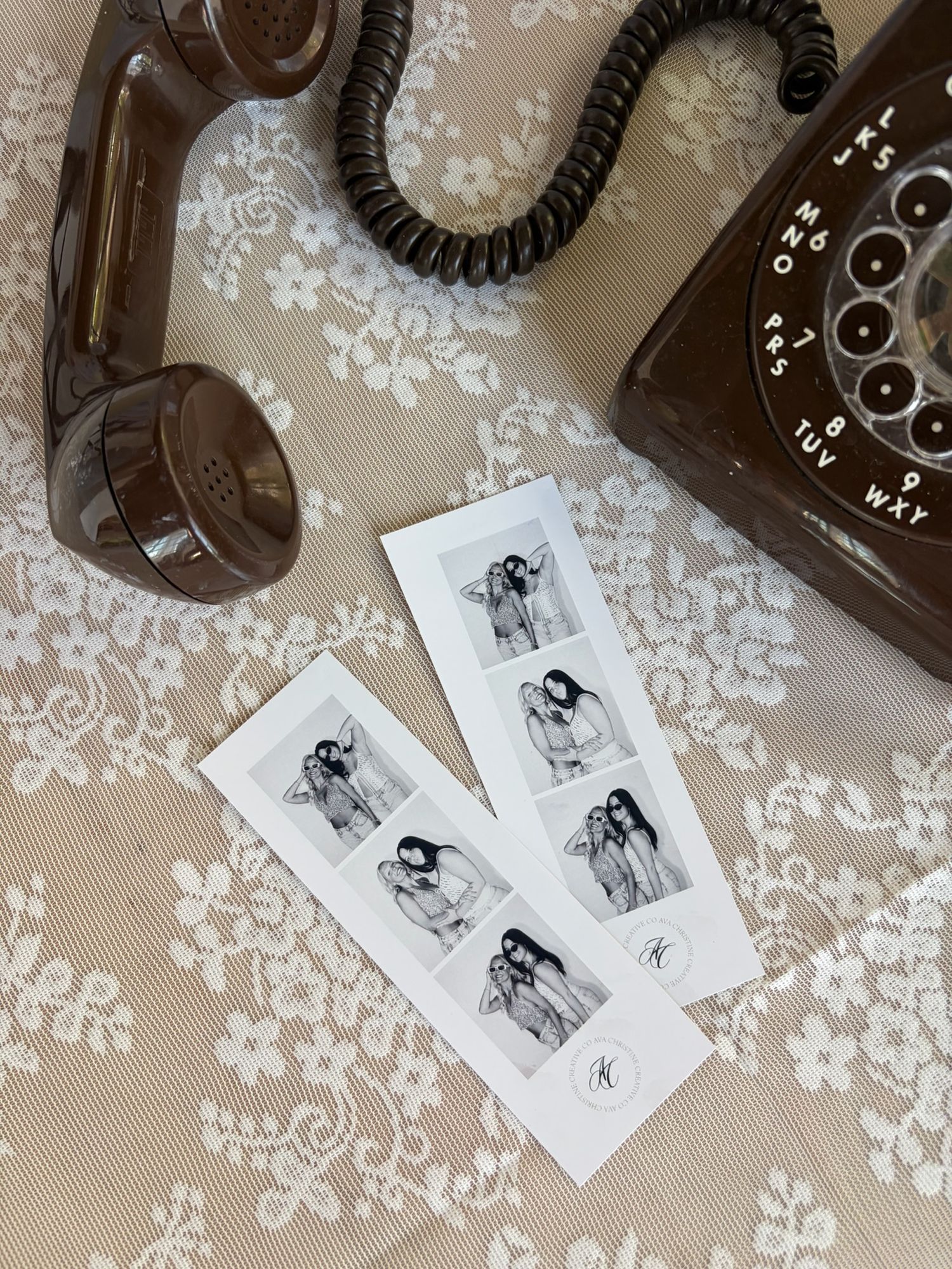 Black and white photo booth strips beside a vintage rotary telephone on floral lace fabric.