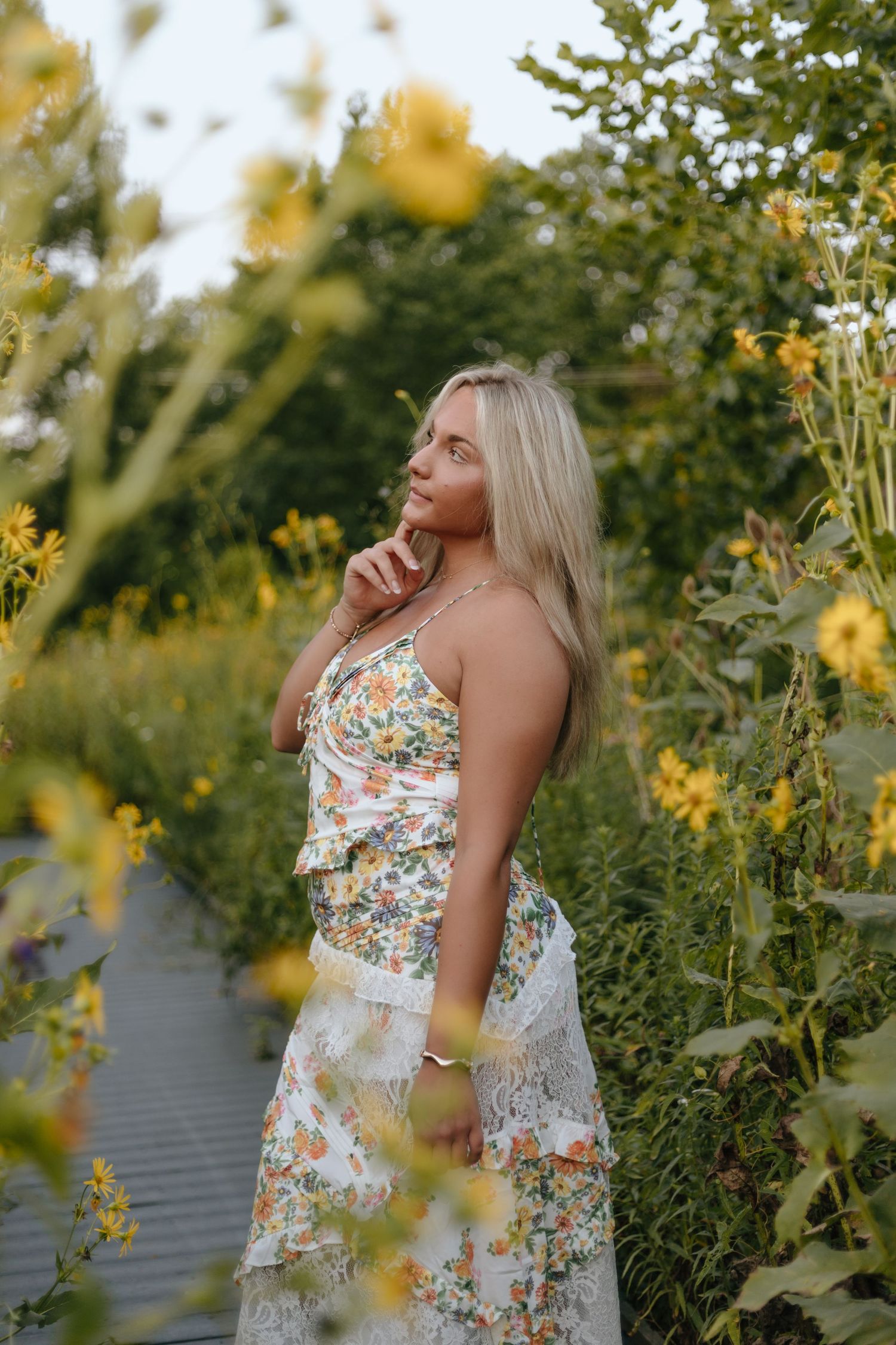 Summer portrait among yellow wildflowers with floral dress on wooden boardwalk.