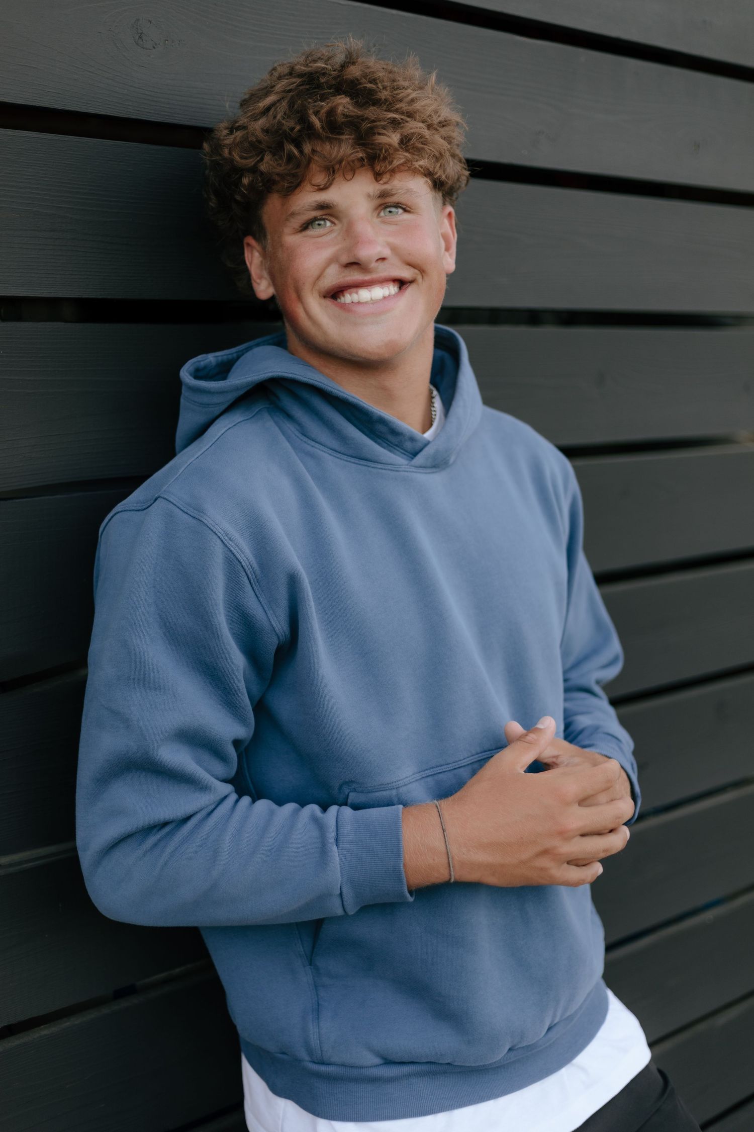 Person in a light blue hoodie smiling against dark wall background.