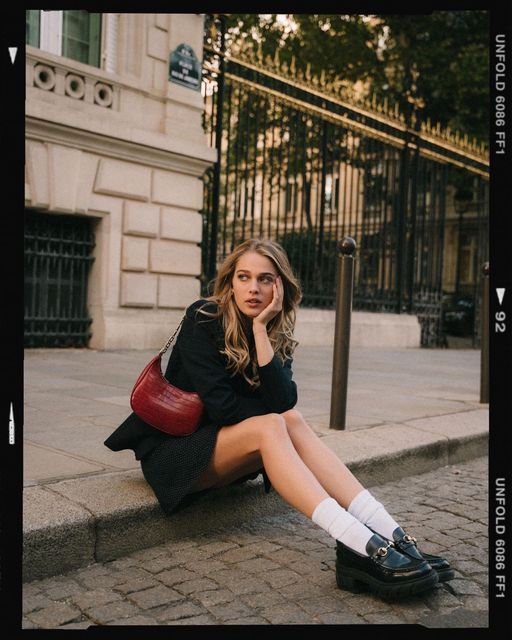 Person in black outfit and white socks sitting on sidewalk next to ornate building with multiple poses.