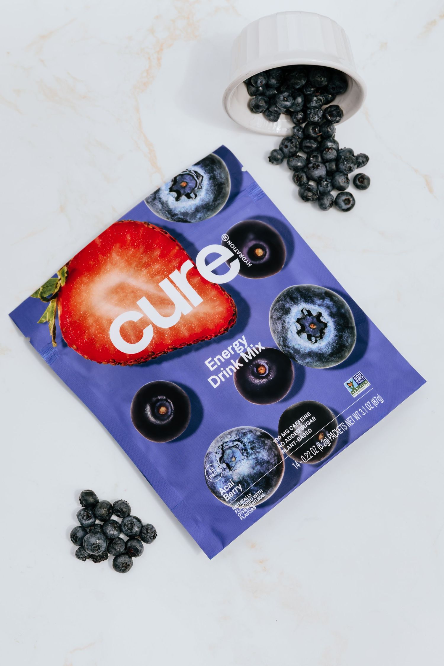 Cure hydration packets with fresh blueberries and strawberries scattered on marble surface.