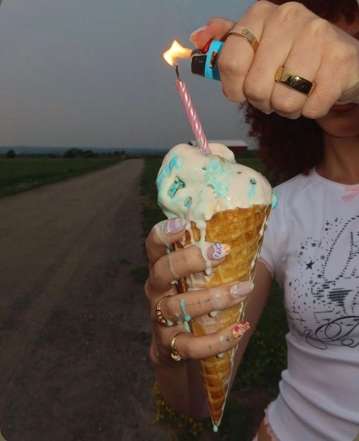Person holding a large waffle cone ice cream while lighting a candle on a rural road at dusk.