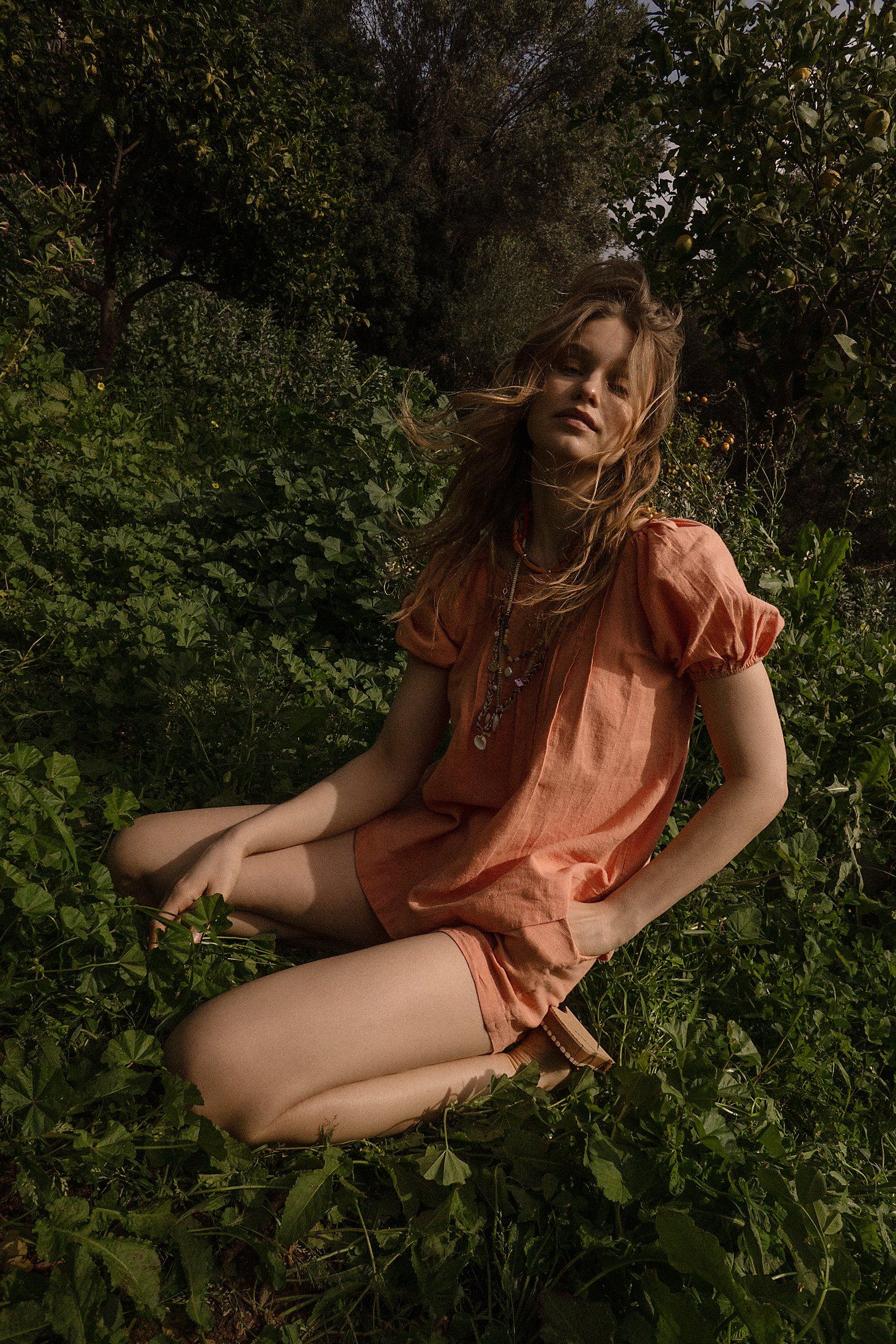 Person in coral dress lying on grass in artistic outdoor photoshoot with natural lighting.