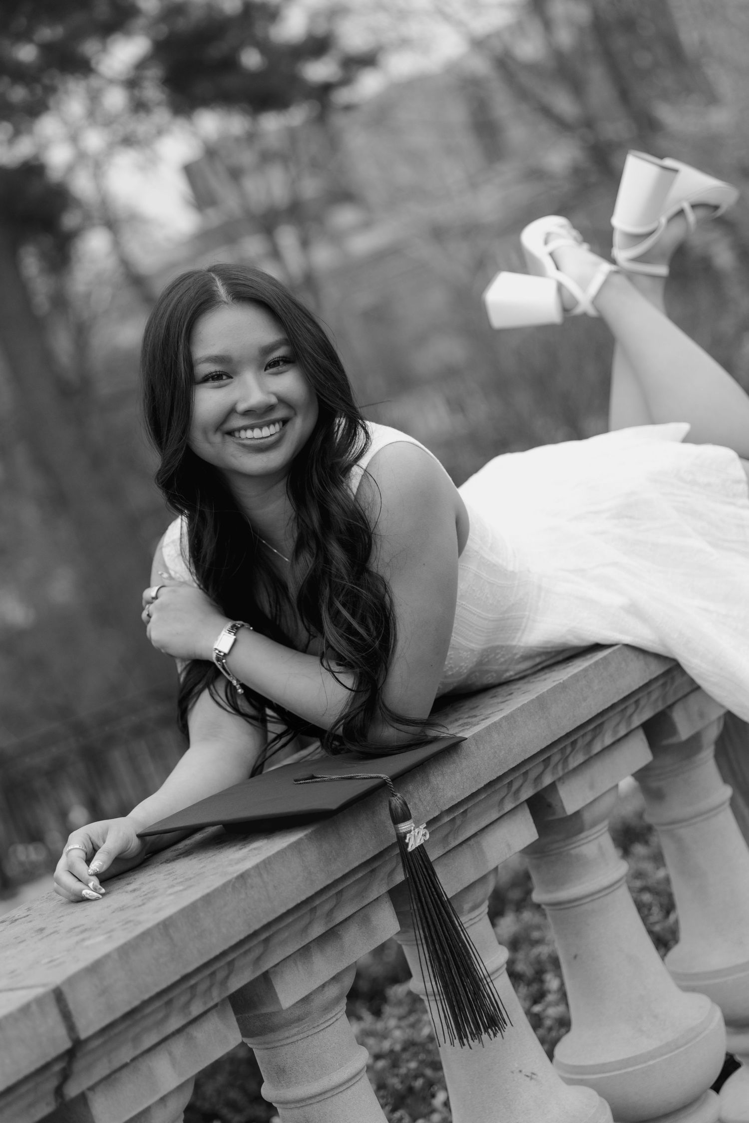Black and white photo series of graduate in formal dress reclining on stone wall outdoors.