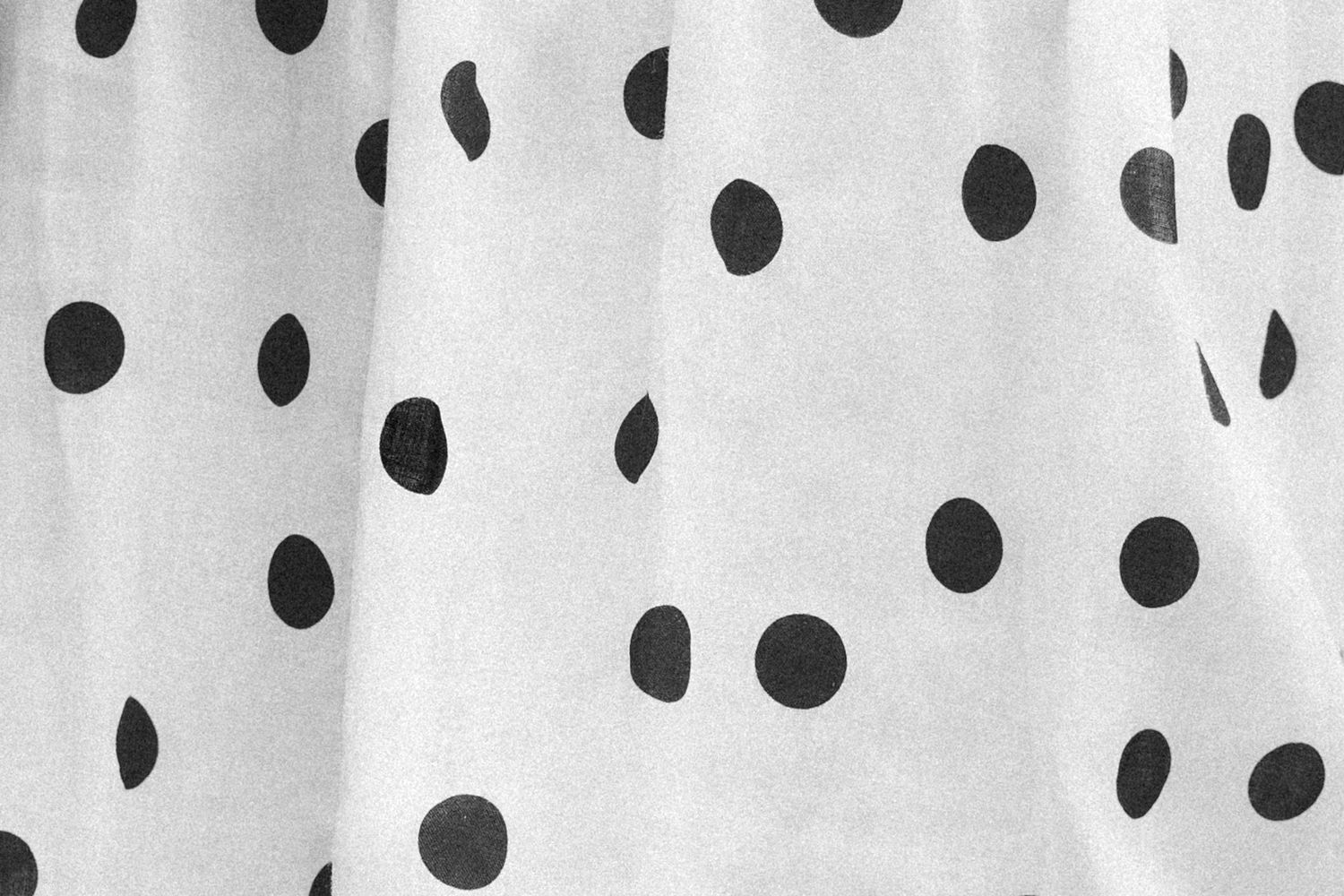 White fabric with black polka dots pattern, featuring soft folds and a classic monochrome design.