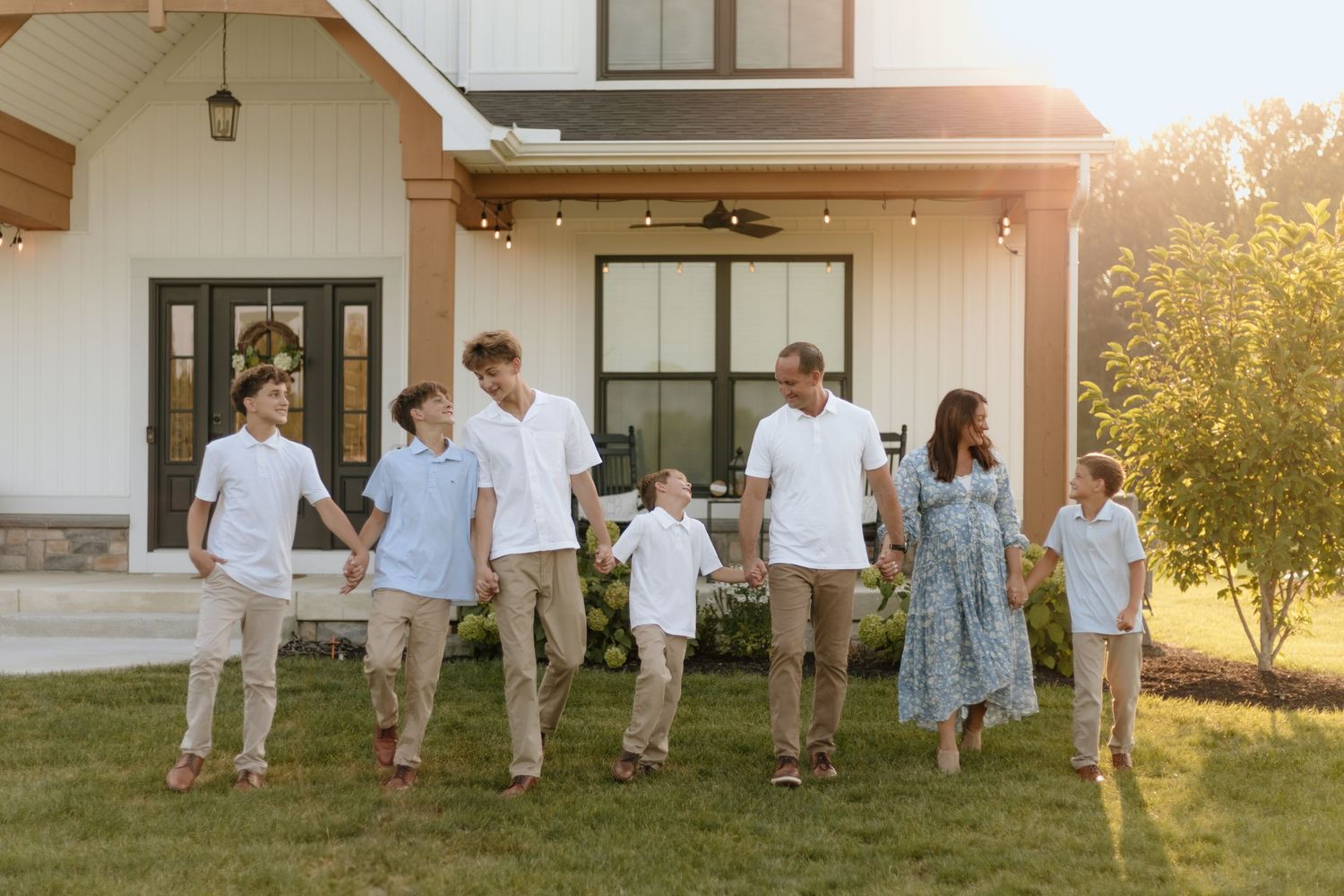 Family gathering photos in coordinated outfits during golden hour against house backdrop.