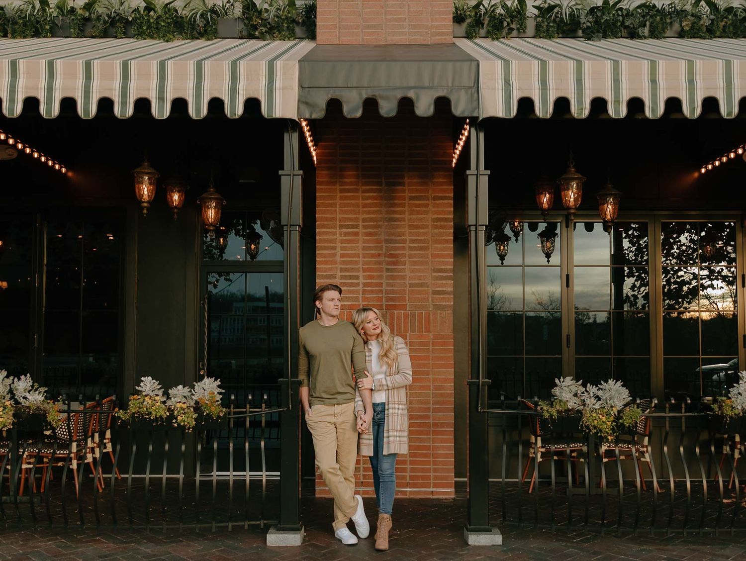 Evening engagement photos outside a brick storefront with string lights and awnings.