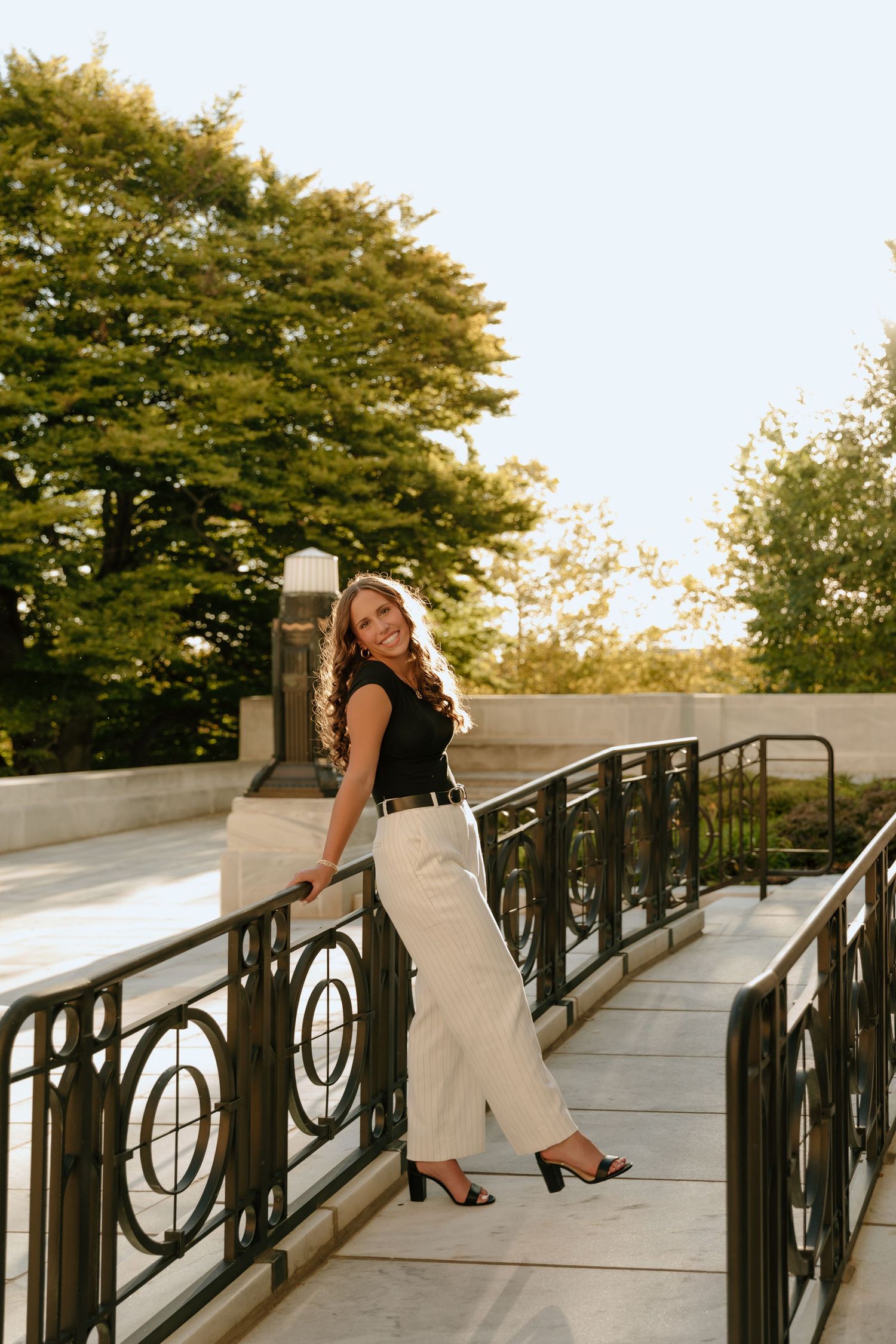 A stylish outfit featuring a black top and white pants photographed on an elegant outdoor staircase at sunset.
