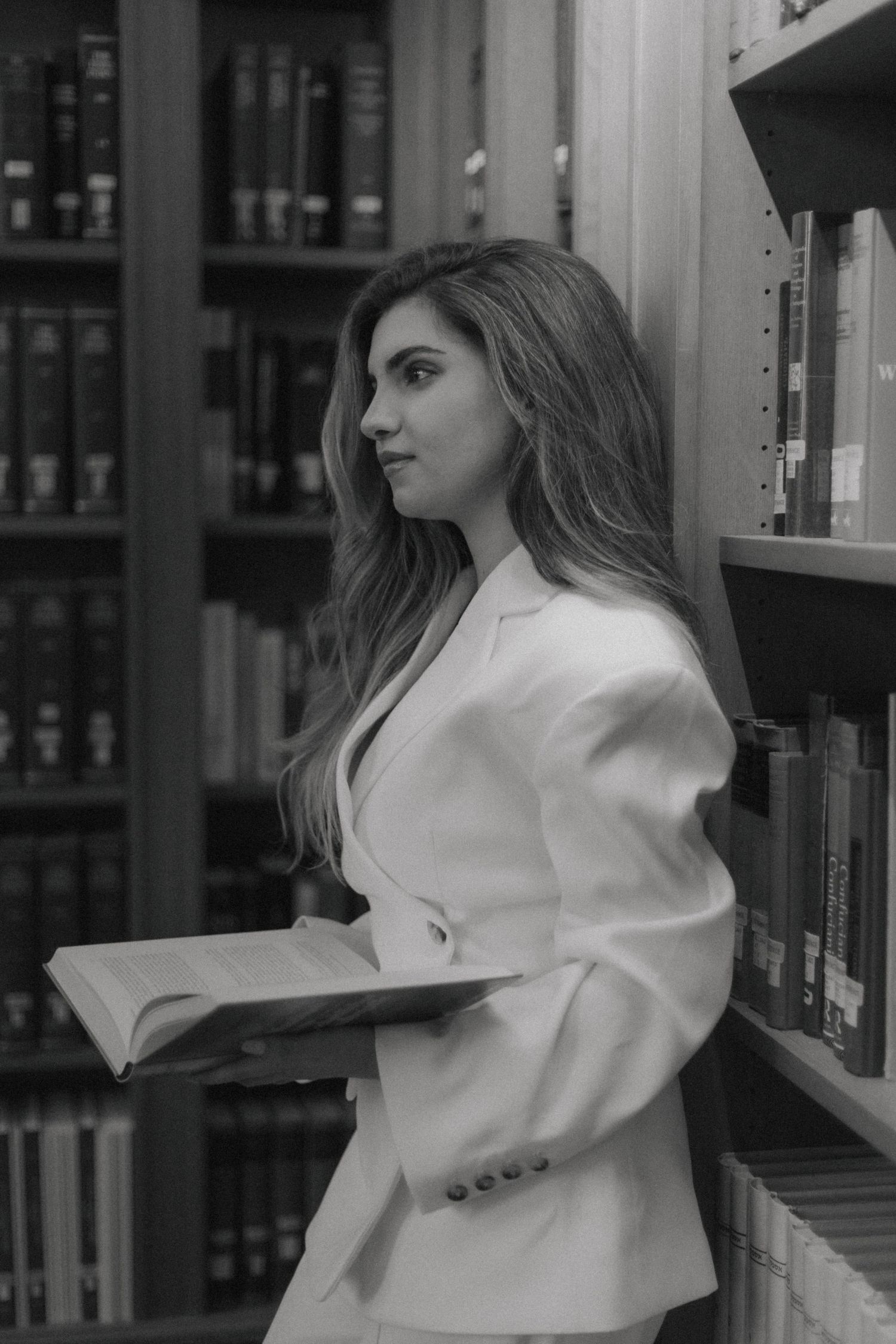 A person in a white blazer stands between library bookshelves in a black and white photograph.
