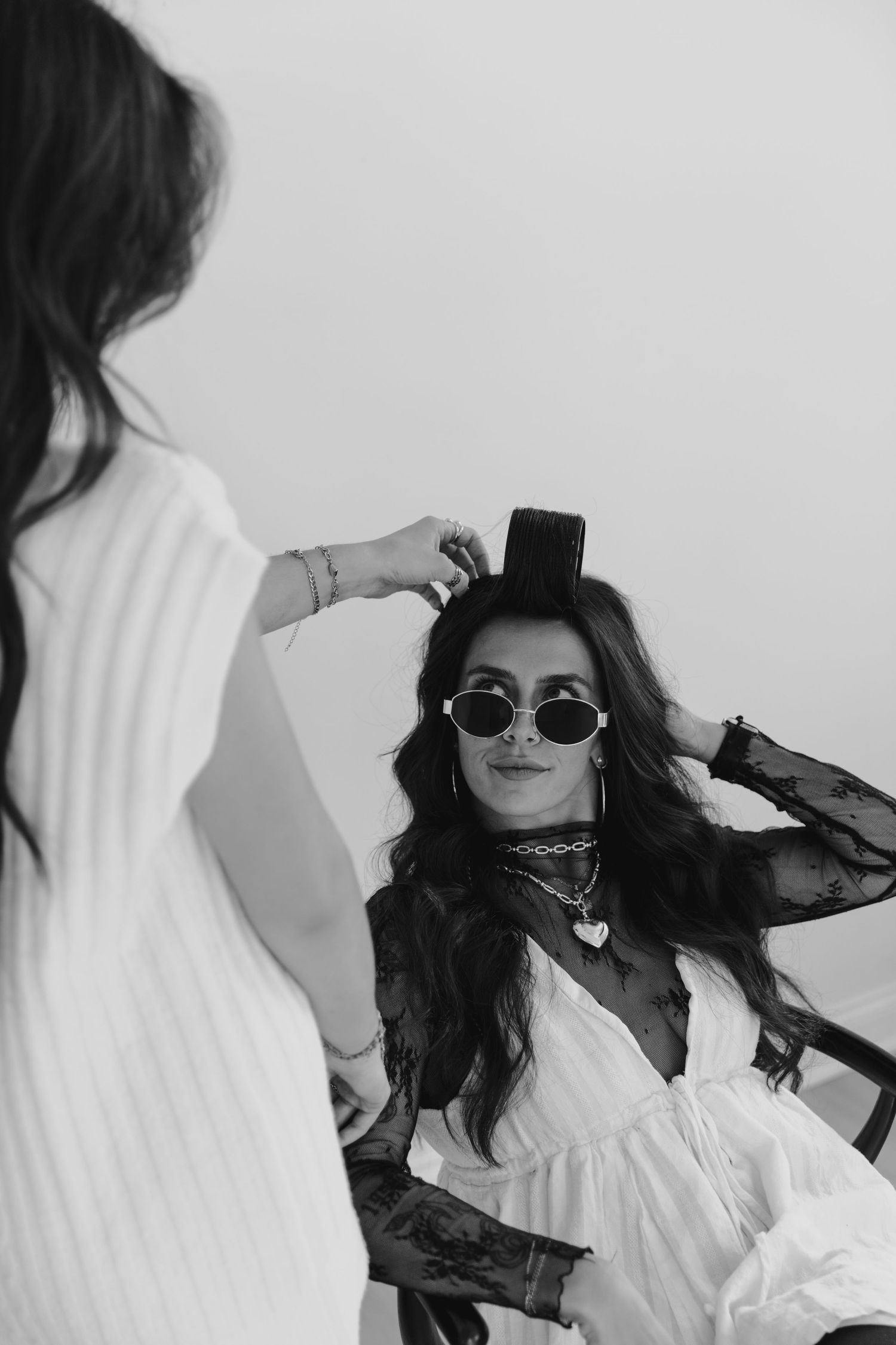 Black and white photo of someone in a white dress and sunglasses having their hair styled during a photoshoot.