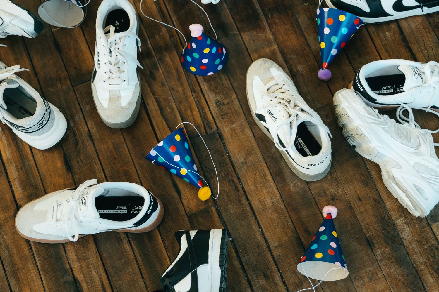 White sneakers and colorful polka dot party hats scattered on a rustic wooden floor.
