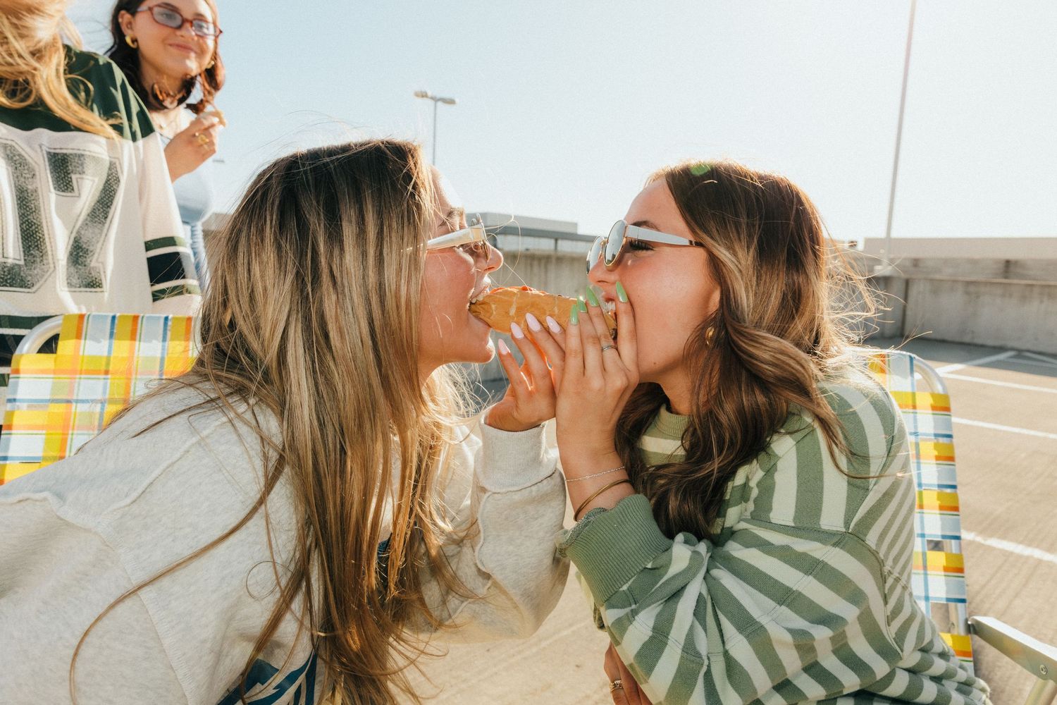 Two young women sharing a burger outdoors on a sunny day, laughing and enjoying food together.