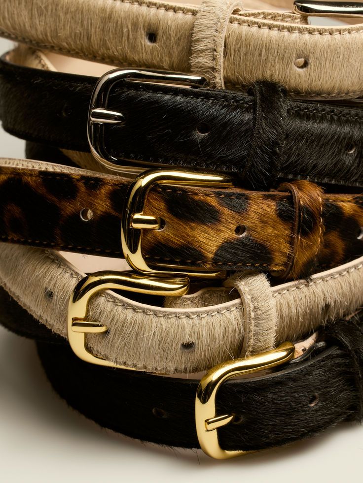 Close-up view of cowhide leather belts with brass buckles showing natural fur texture and patterns.