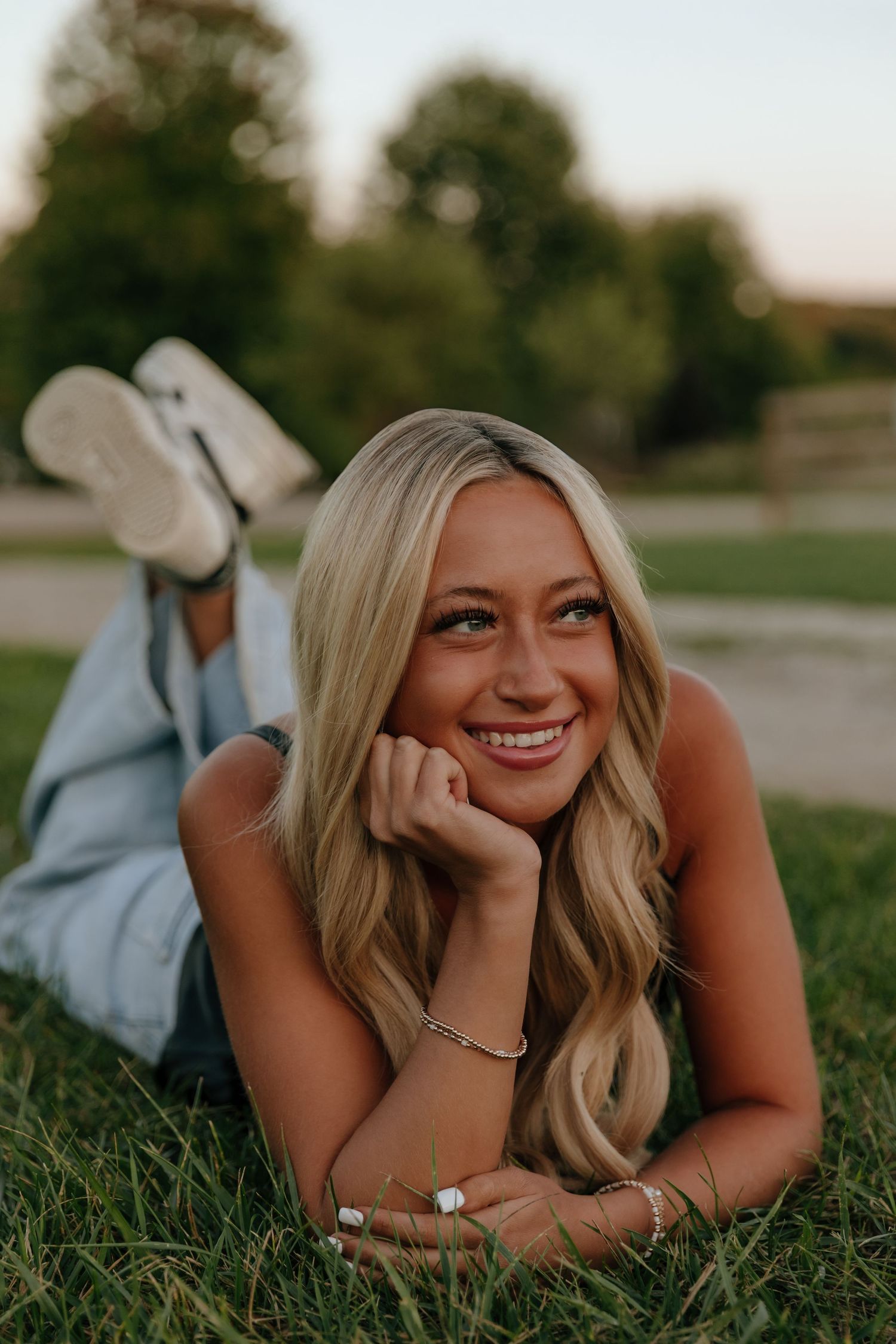 A person lies on green grass during a golden hour photoshoot, creating a relaxed and joyful outdoor portrait.