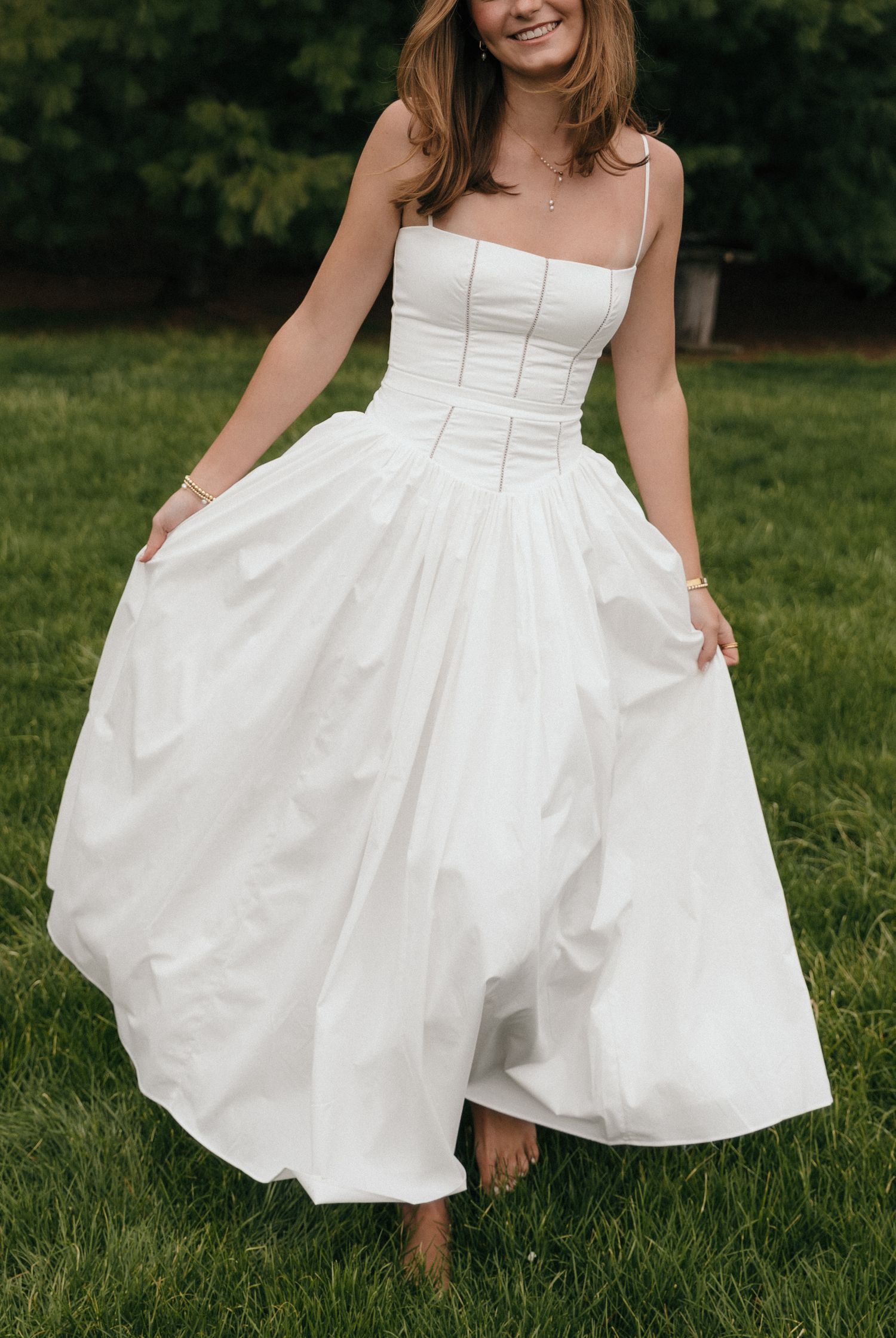 Bride twirling in white corset bodice ball gown wedding dress on green lawn.