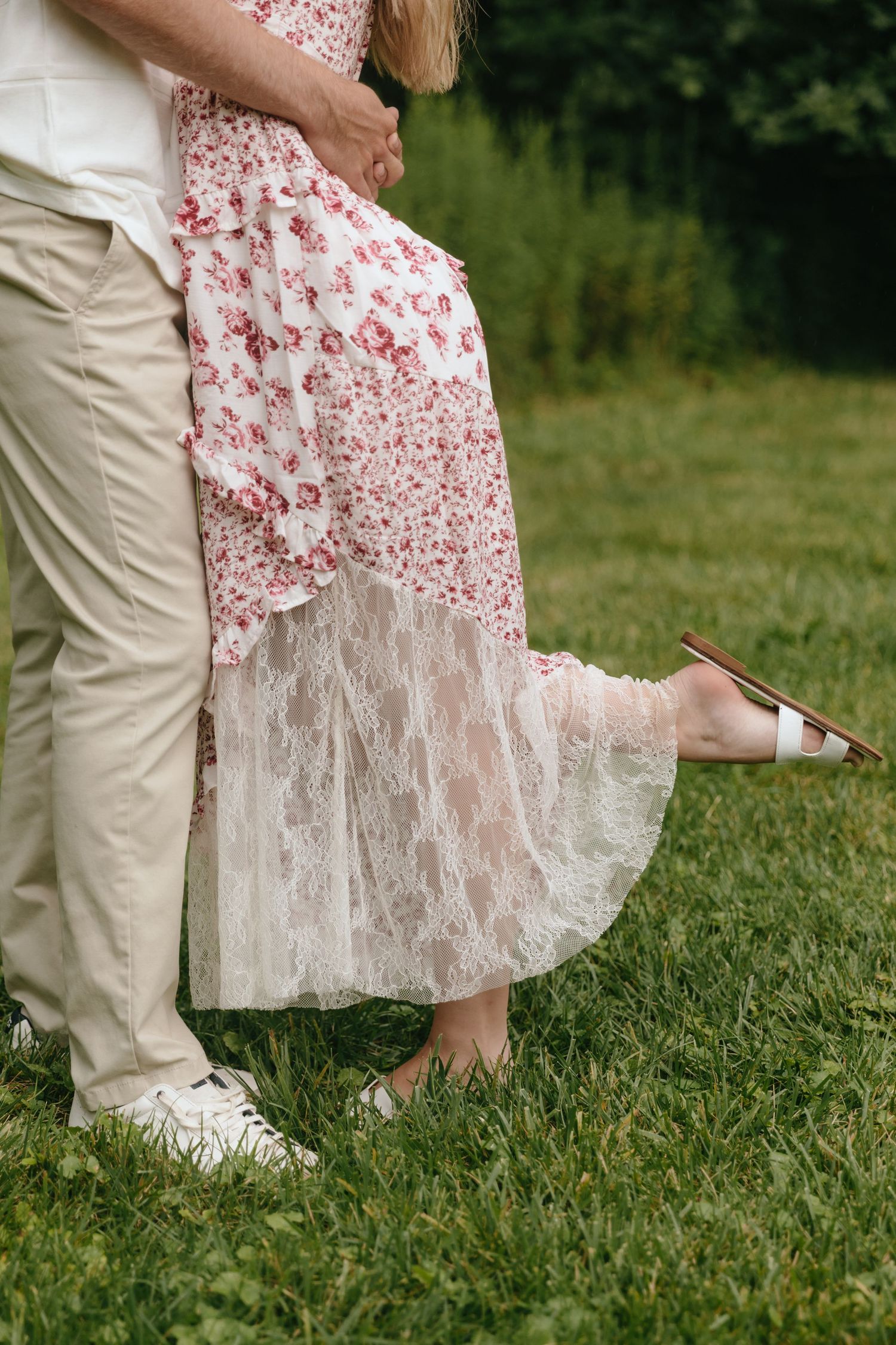 Detail shot of floral dress and casual footwear on green grass.