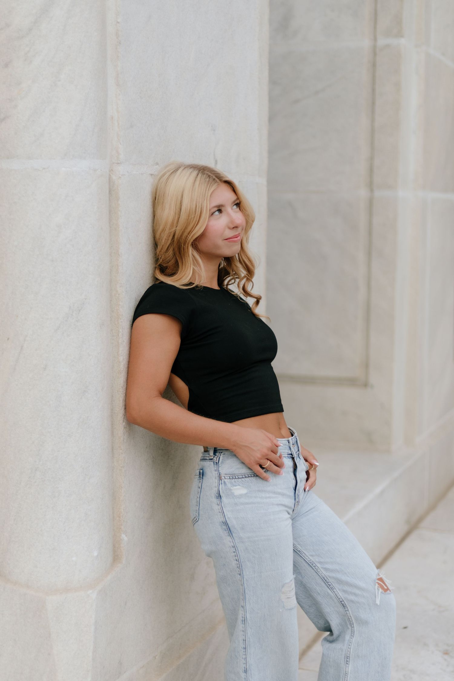 Style portraits against white marble wall wearing black top and light jeans.