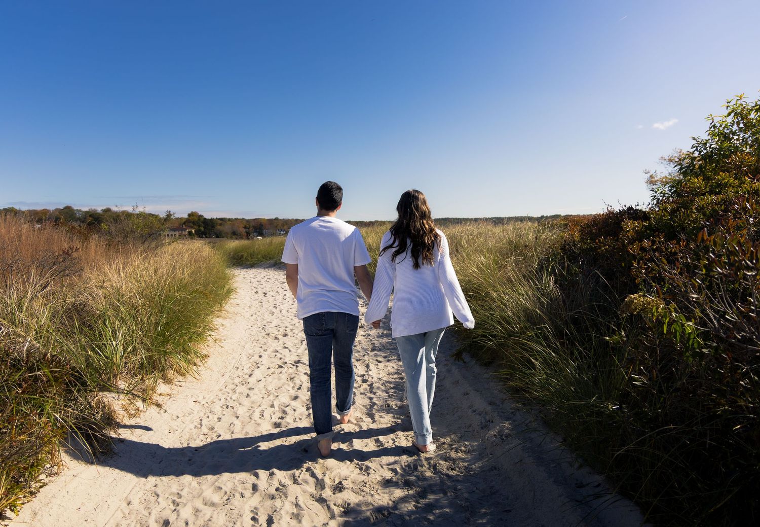 Warm beach engagement photoshoot with couple holding hands, includes a gorgeous landscape and sky