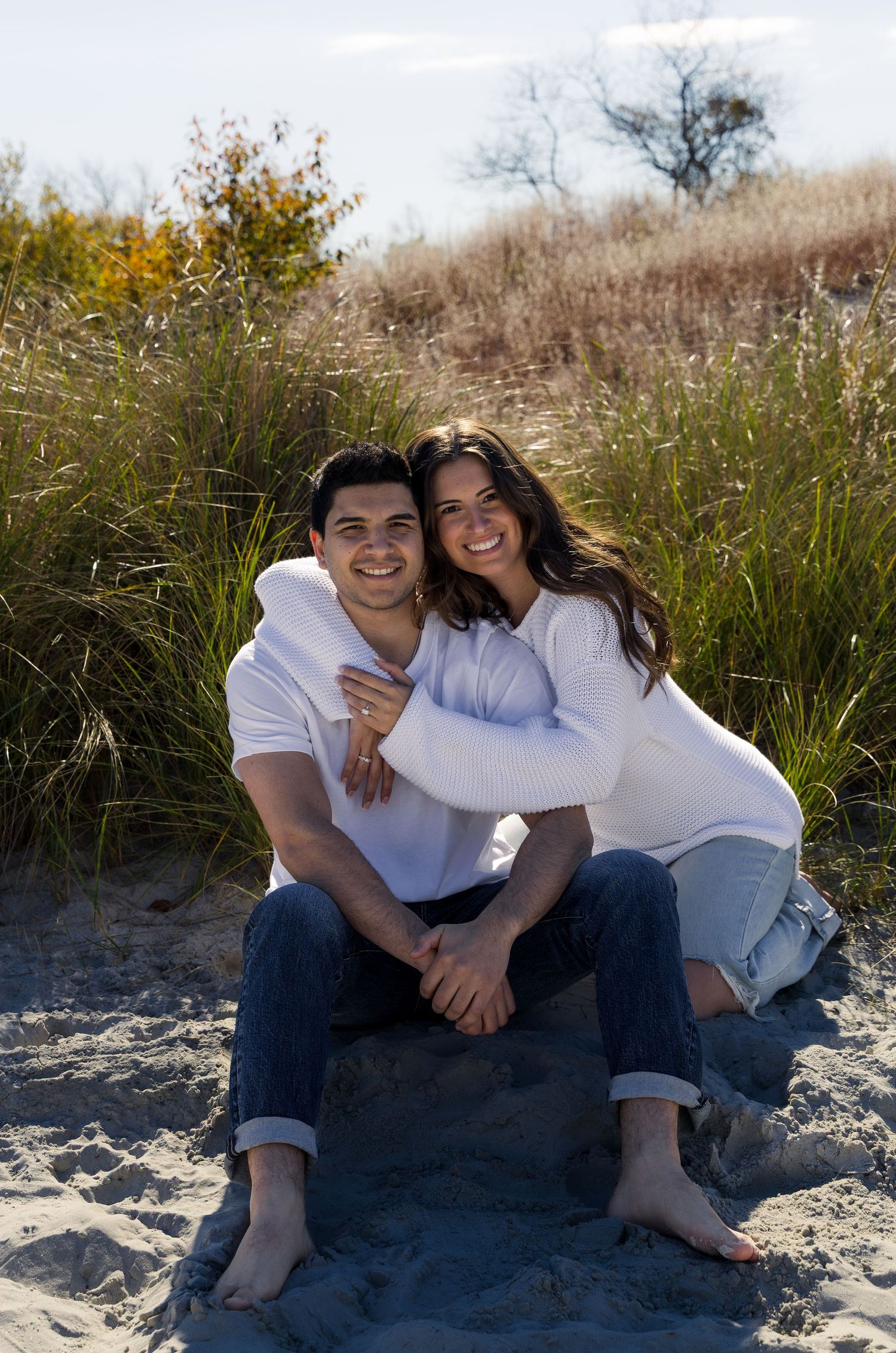 Outdoor beach engagement photoshoot featuring smiling couple wrapped in each others arms