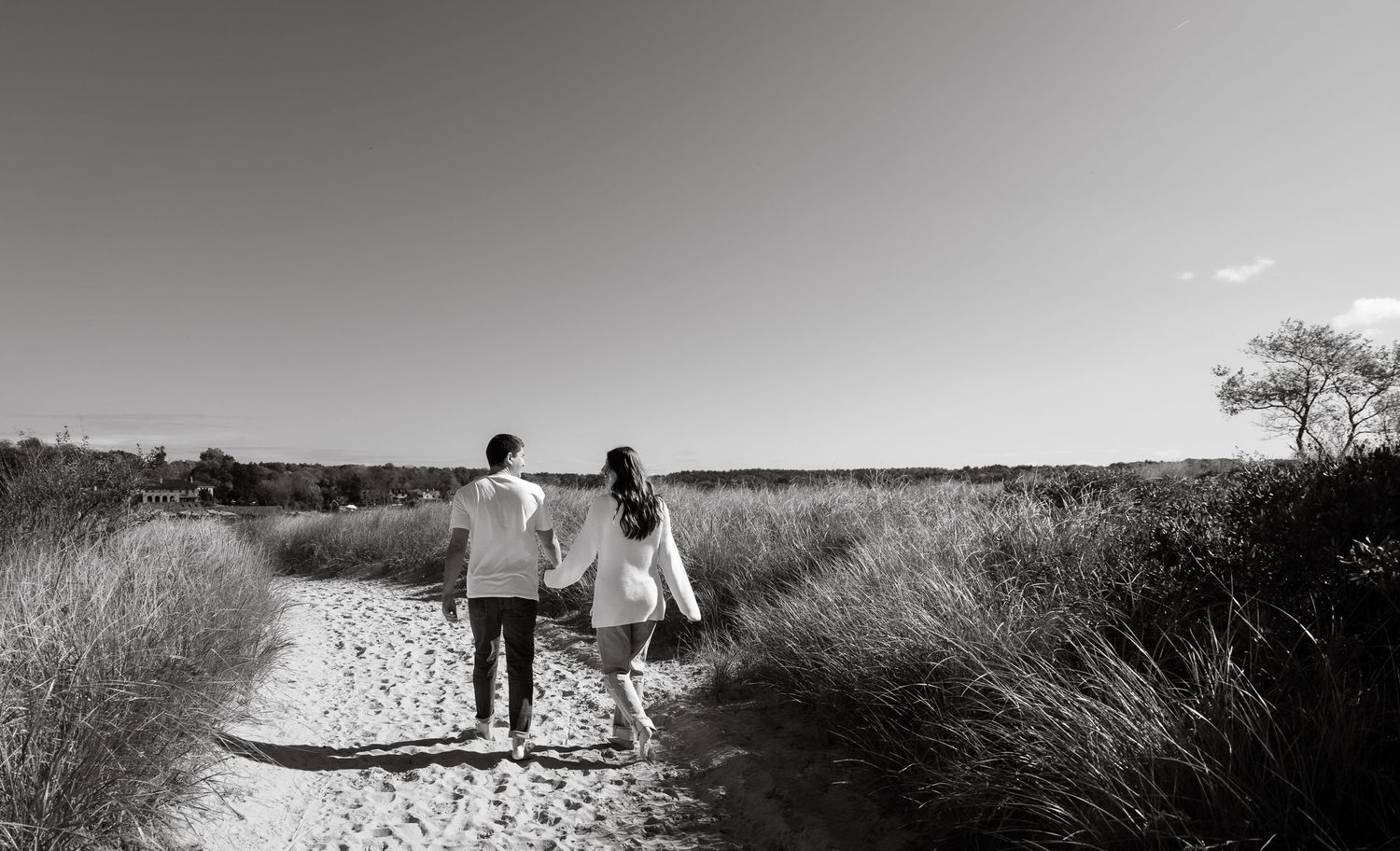 Black and white beach engagement photoshoot with couple holding hands, includes a gorgeous landscape and sky
