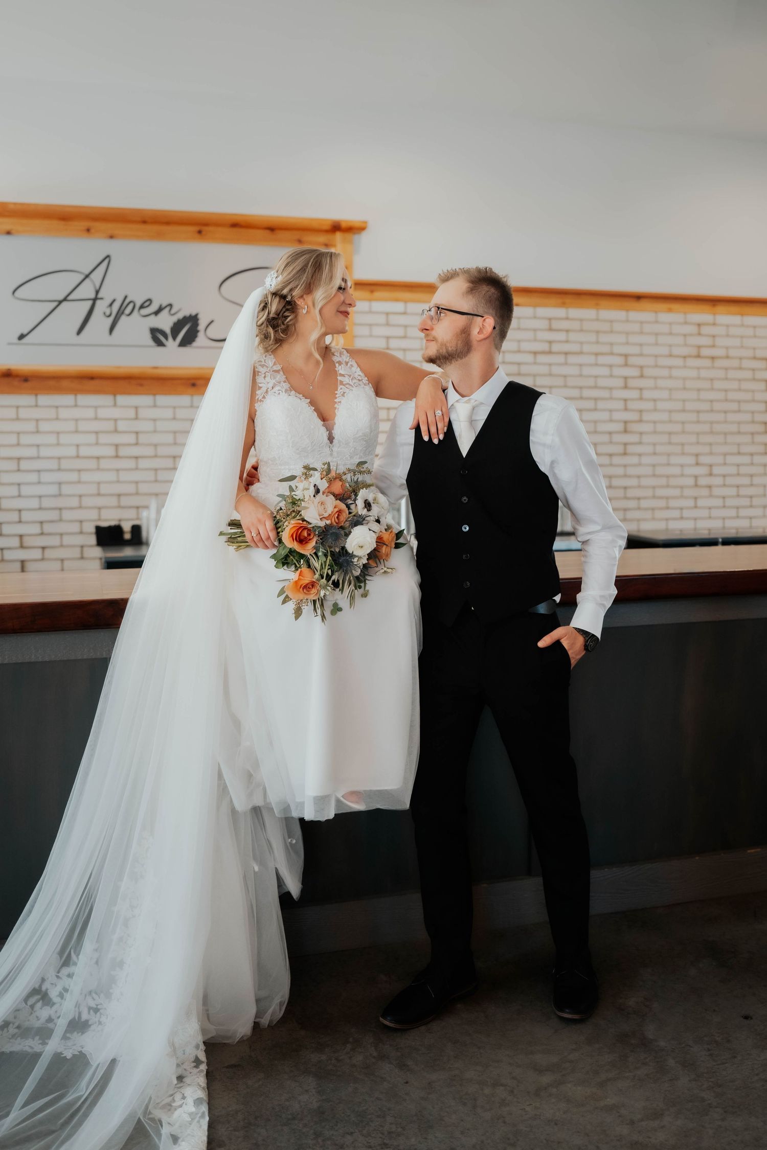 Bride and groom share a tender moment indoors at Aspen venue, she holding orange and white bouquet.