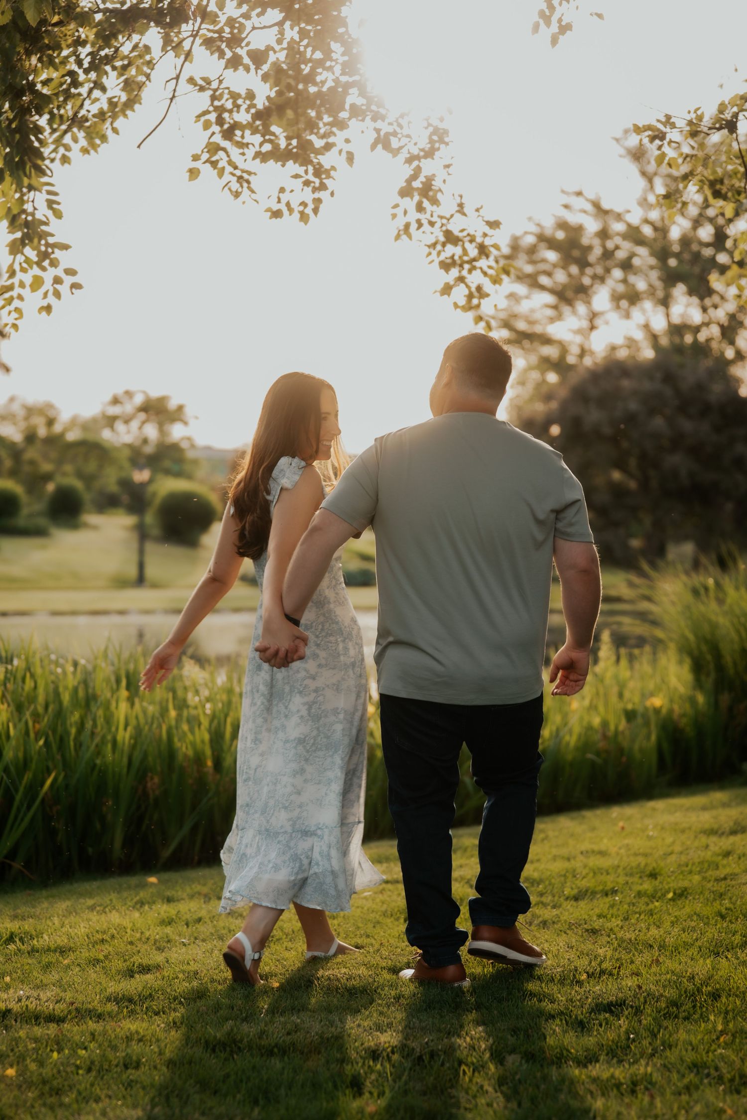 Couple strolling hand in hand through a sunlit garden at golden hour, viewed from behind.