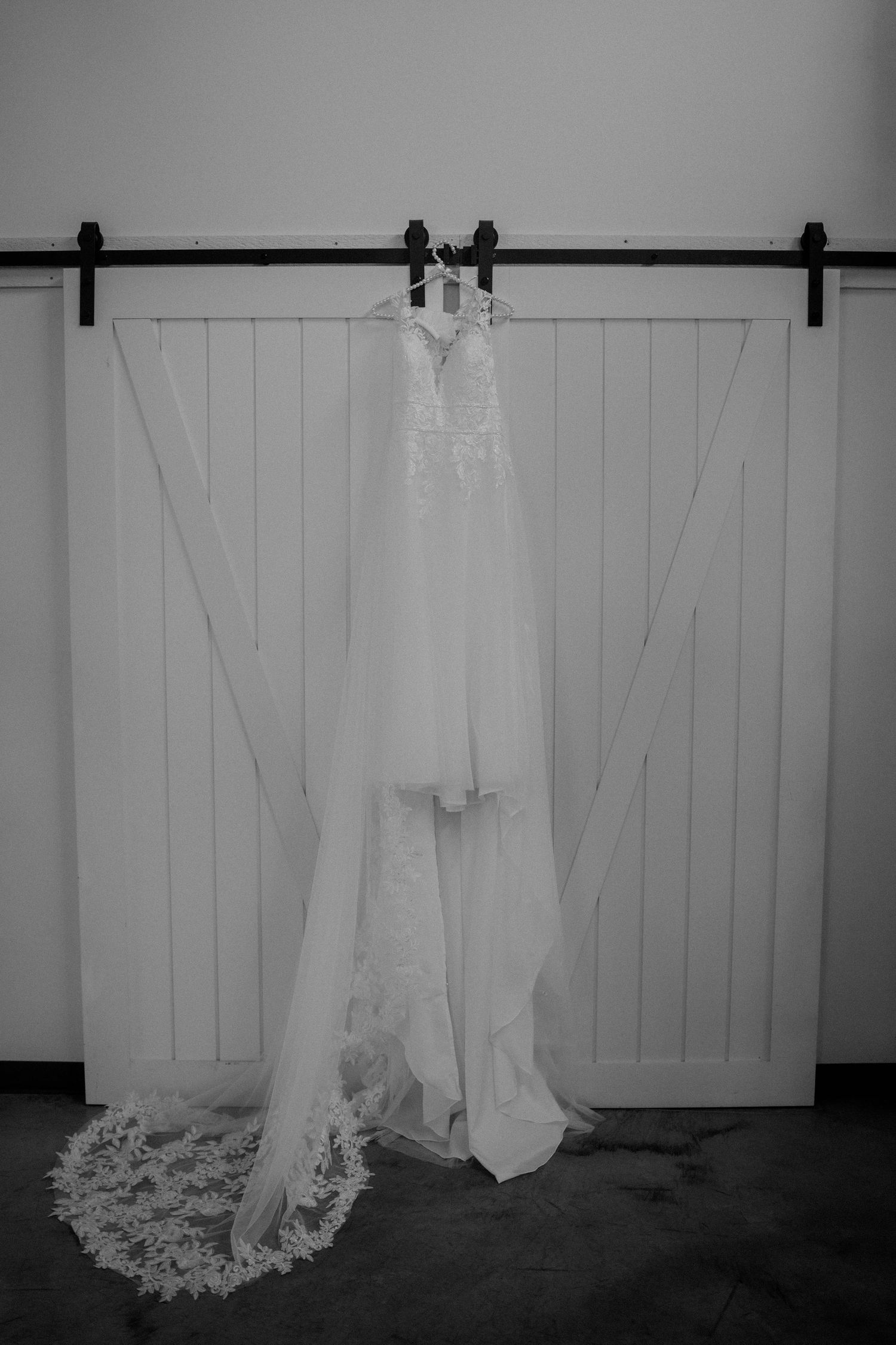 Black and white photo of a lace wedding gown hanging on a white barn sliding door.