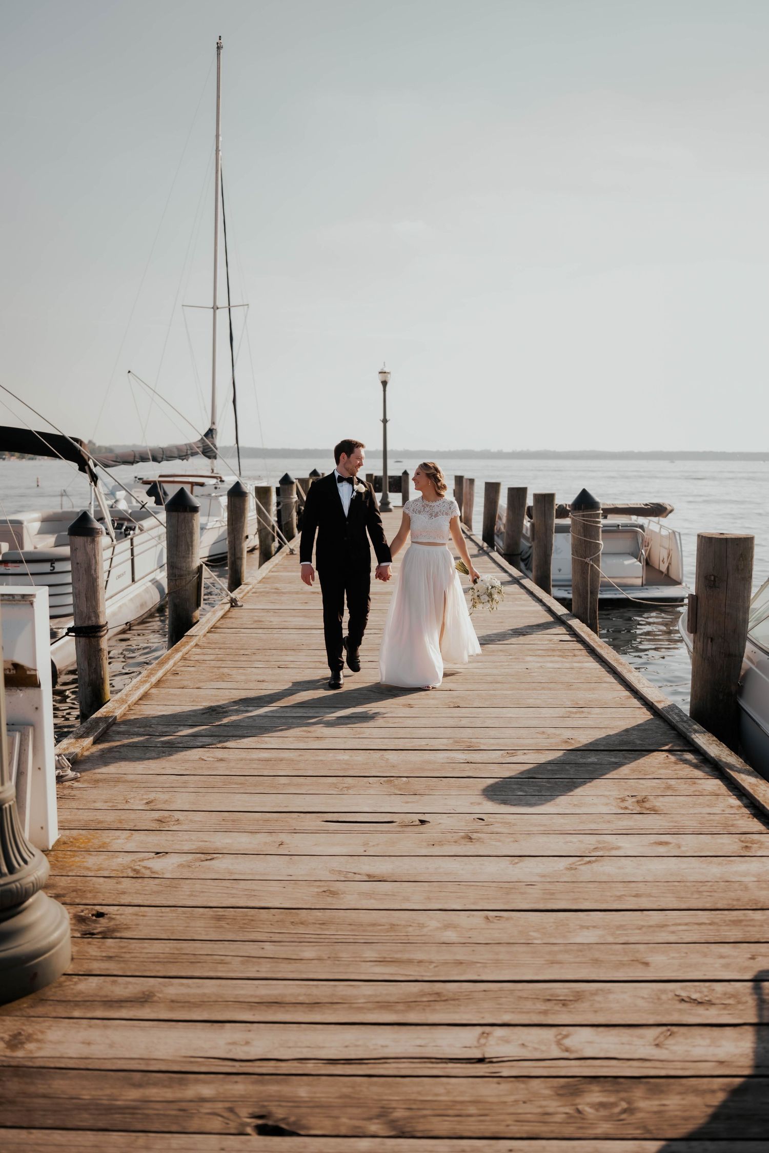 Bride and groom strolling hand in hand on scenic waterfront boardwalk.