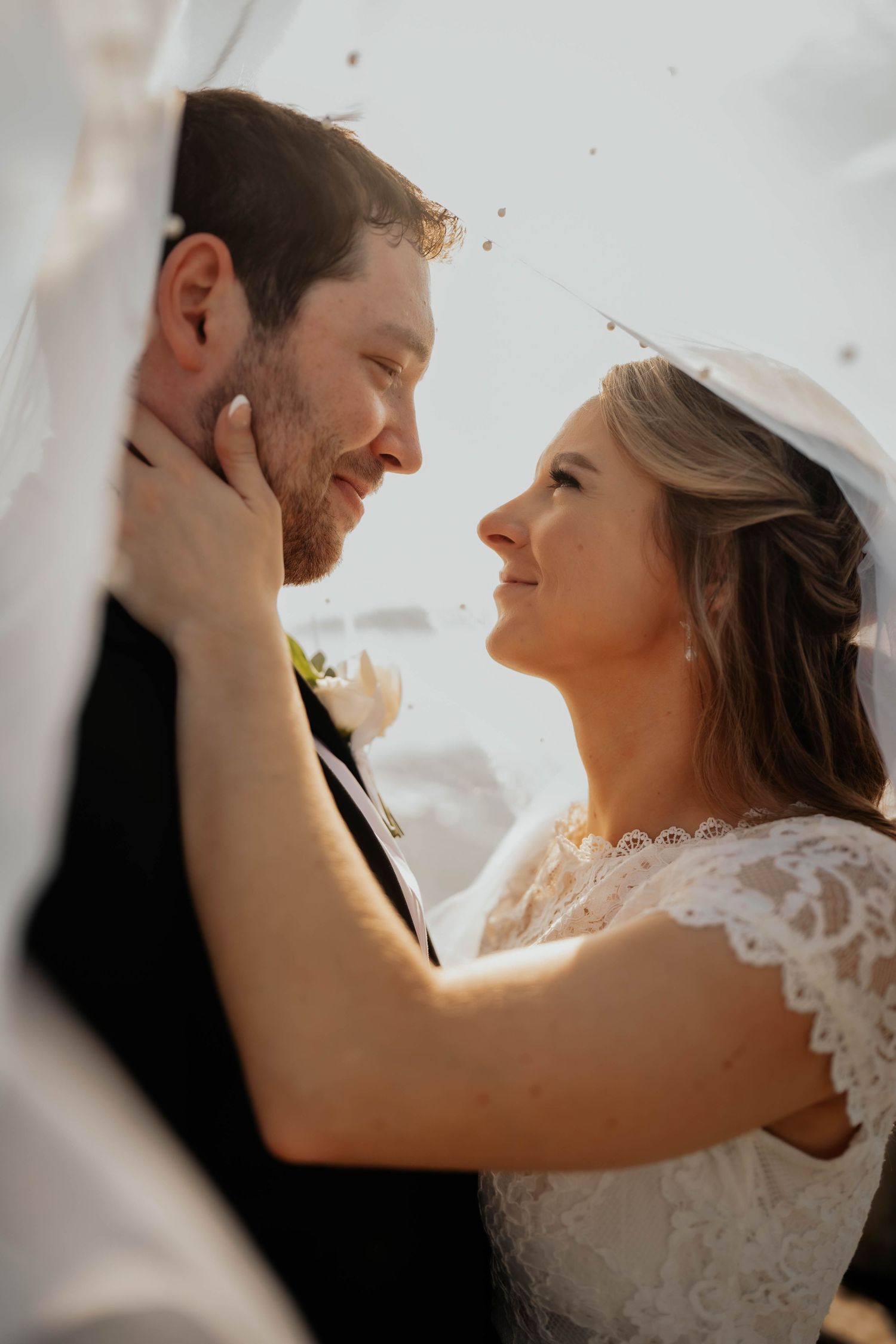 Romantic close-up of bride and groom gazing at each other tenderly in warm golden light.