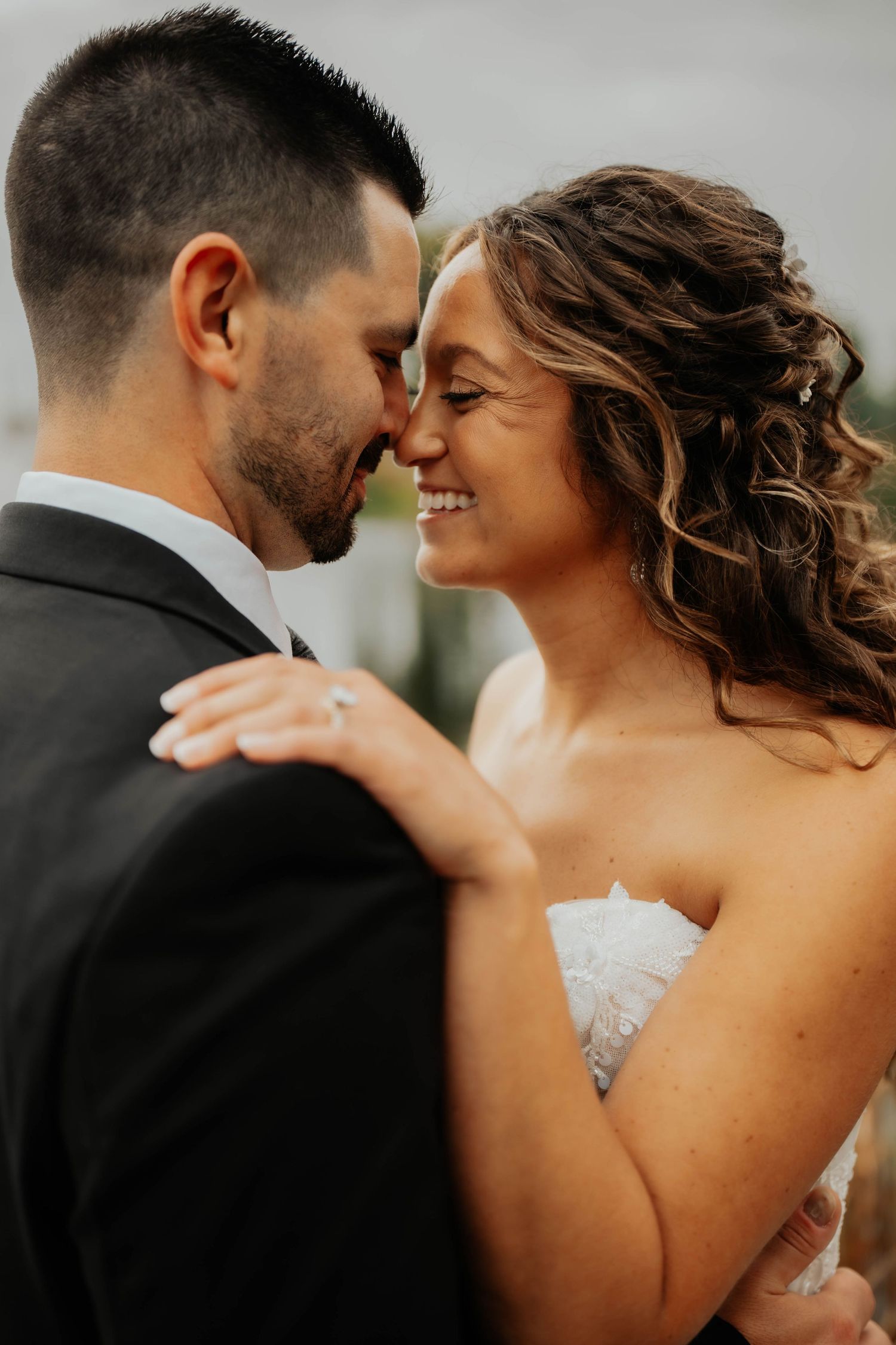 Smiling bride with curly hair touching foreheads with groom during romantic outdoor wedding portraits.
