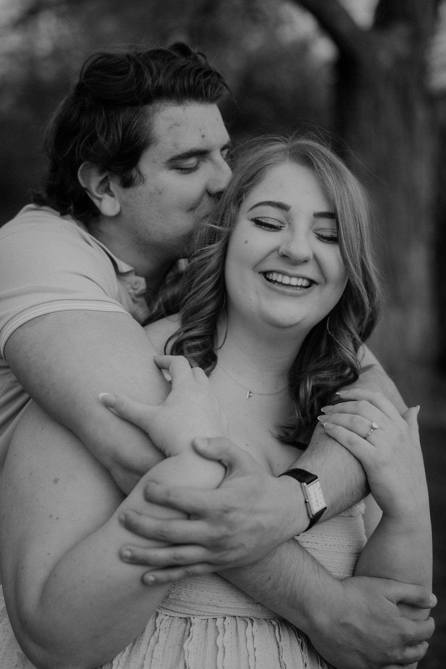 Black and white photo of man kissing woman's cheek while embracing her.