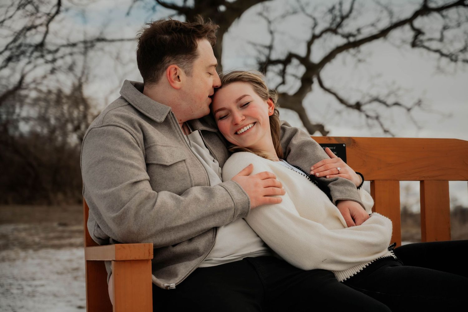 Couple sitting on a bench, man kissing woman's cheek in winter.